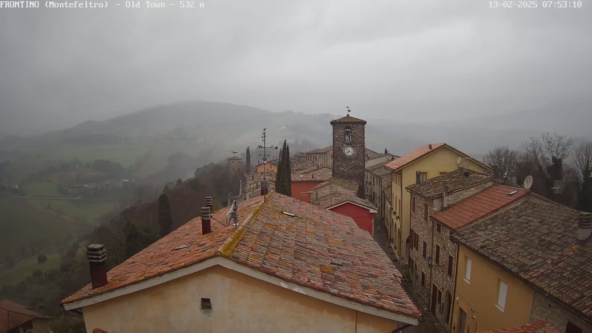 A view of a stone village nestled in a hilly landscape on a foggy day.