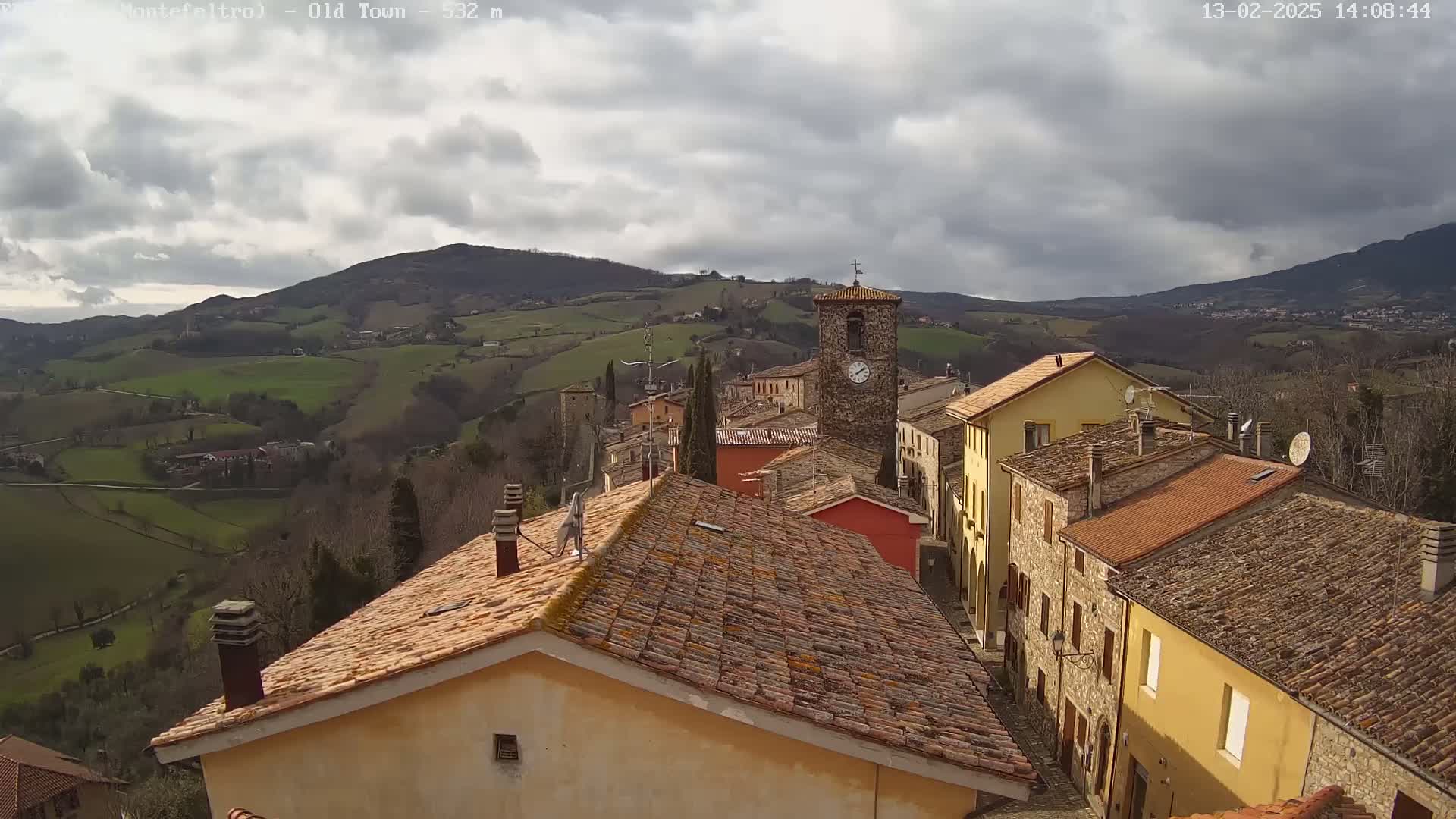 A view from above shows a small town nestled in a valley, with rolling green hills and a cloudy sky.