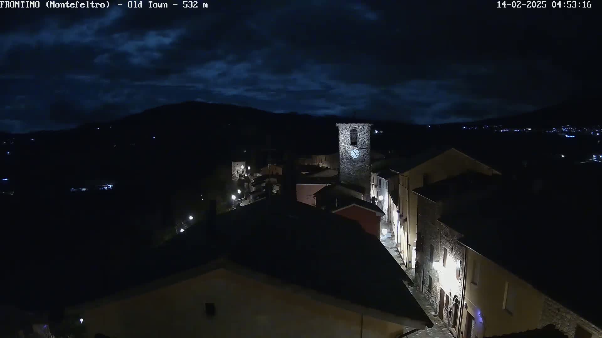 A nighttime, high-angle view of a dimly lit town nestled in a valley under a dark, cloudy sky.