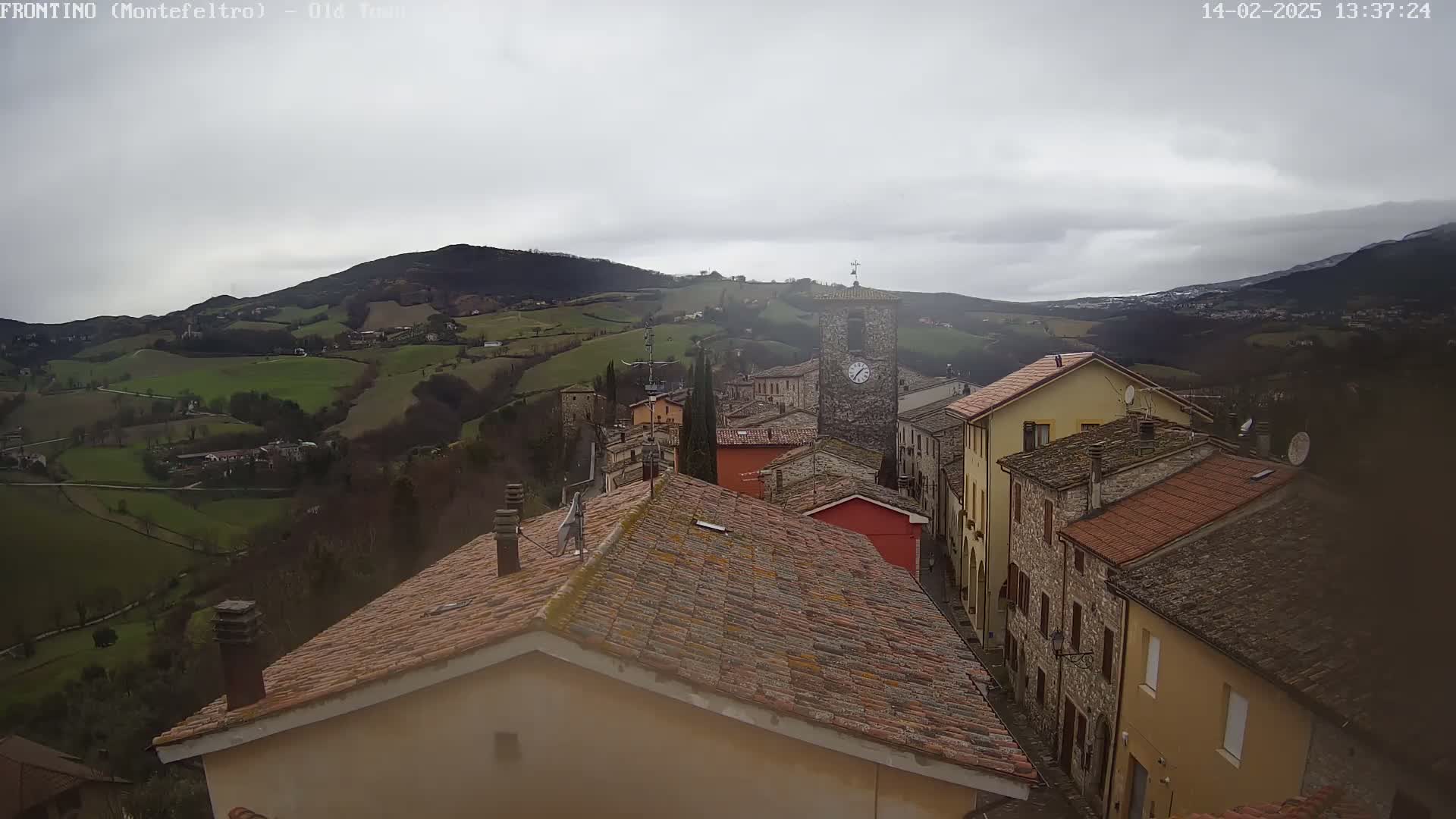 A view from a rooftop shows a stone village nestled in a valley under an overcast sky.