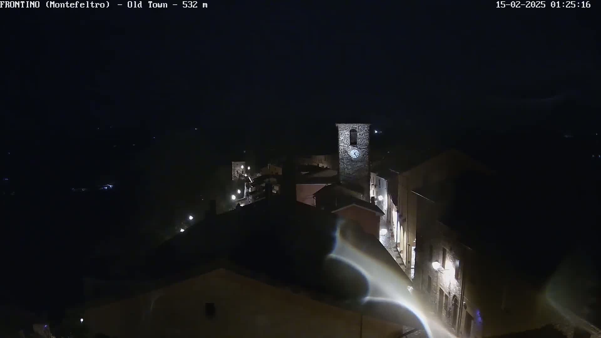 A nighttime, high-angle view shows a small, dimly lit town with a clock tower, under a clear, dark sky.