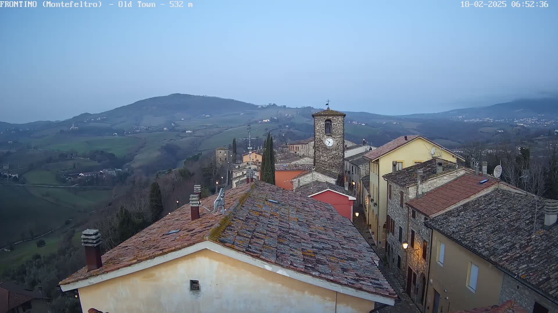 A view of a quaint town nestled in rolling hills under a clear, twilight sky.