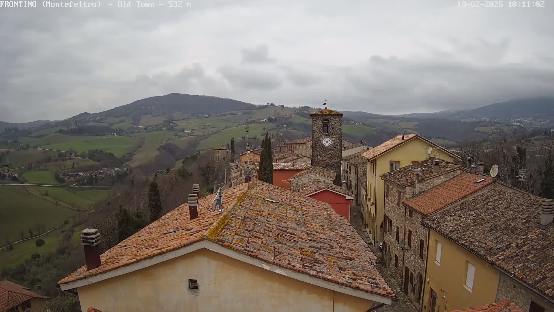 A view of a town nestled in rolling green hills under a cloudy sky.