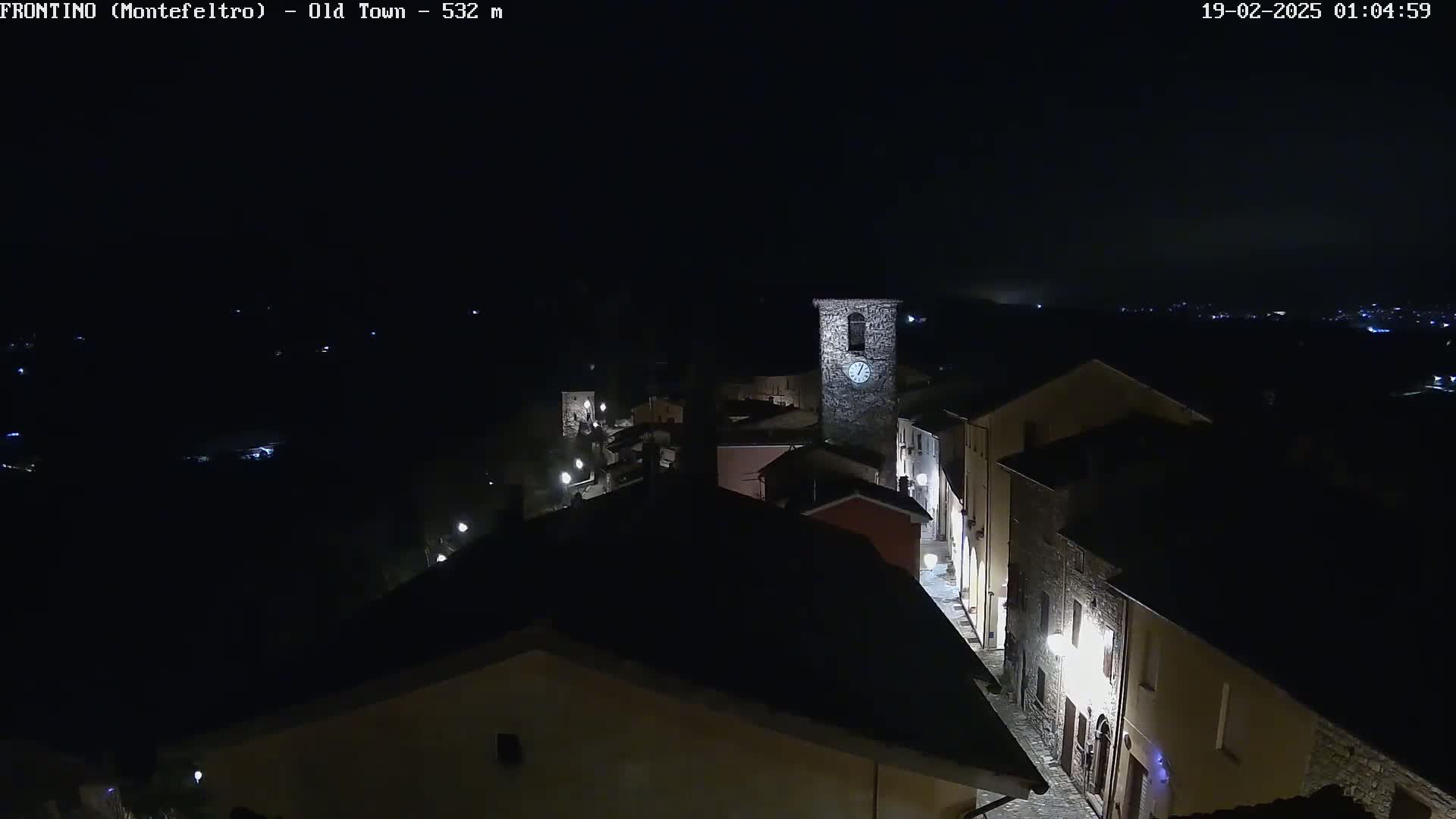 A nighttime, high-angle view of a small, stone village with dimly lit streets and a clock tower.