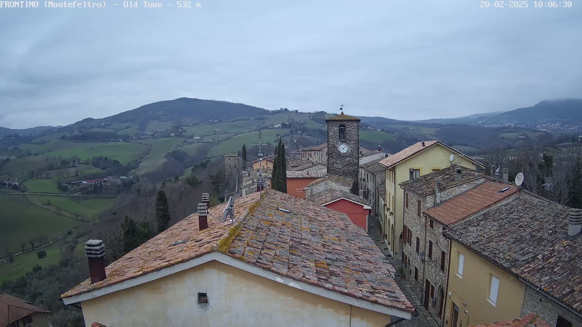 A view from a rooftop shows a quaint village nestled in a hilly landscape under a cloudy sky.