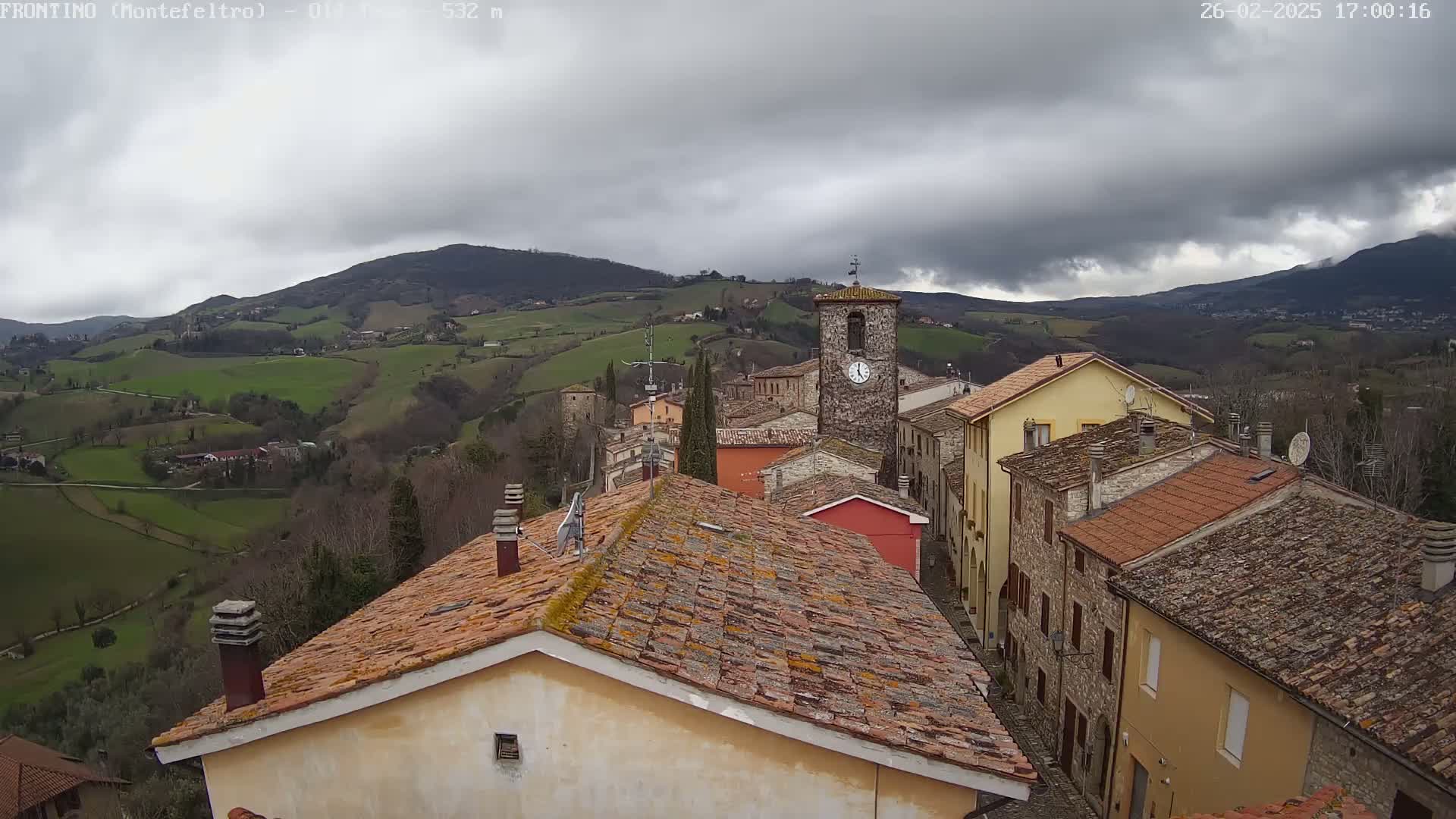 A view of a small town nestled in rolling green hills under a cloudy sky.