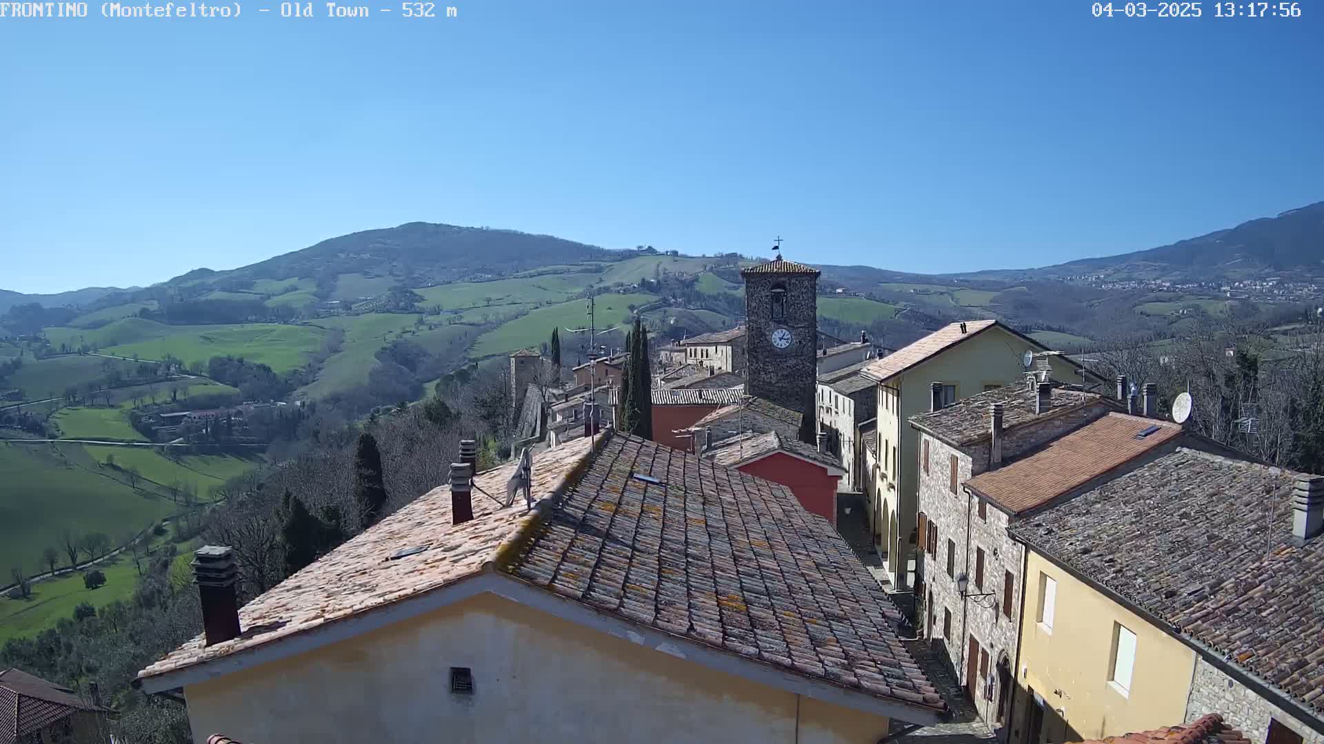 A small village nestled in a valley under a clear blue sky, surrounded by rolling green hills.