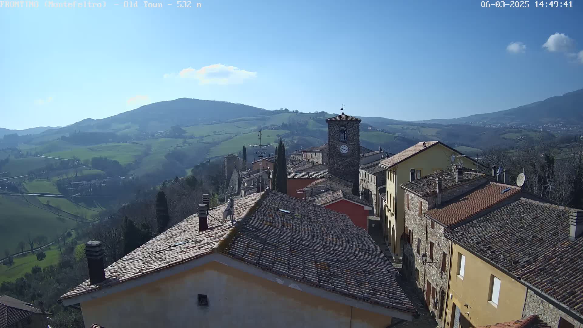 A quaint village nestled in a valley, overlooked by rolling hills under a clear blue sky.