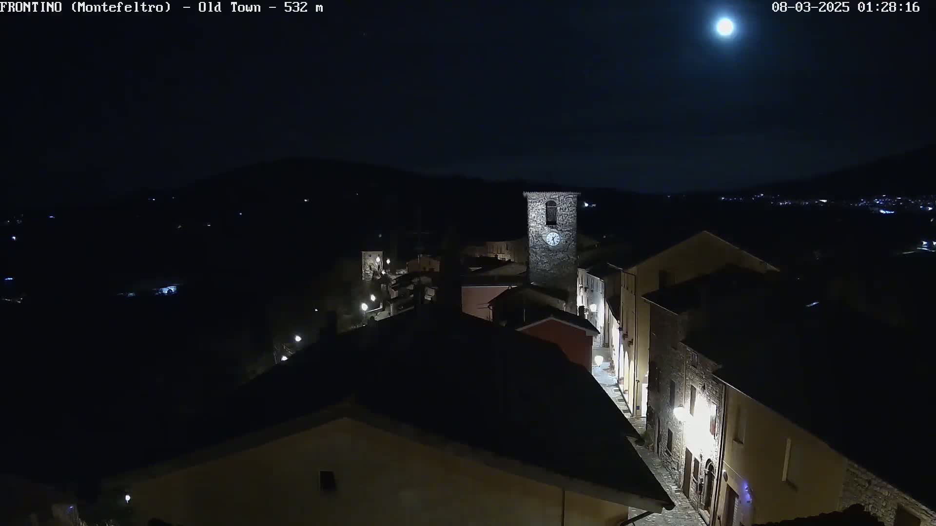 A nighttime, high-angle view shows a small town with a clock tower under a bright moon.
