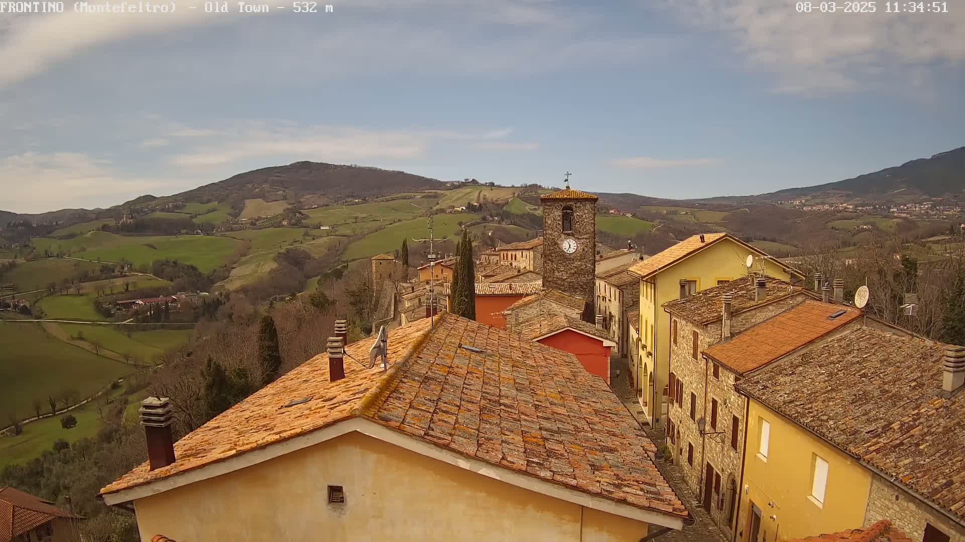 A small village nestled in a valley under a mostly clear sky, surrounded by rolling green hills.