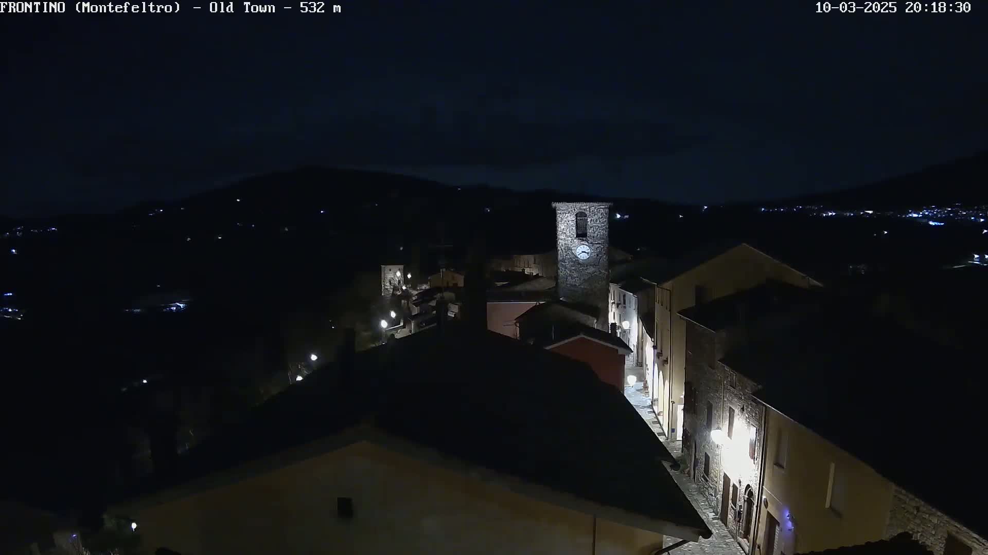 A nighttime, high-angle view of a small, dimly lit town nestled in a dark, hilly landscape.