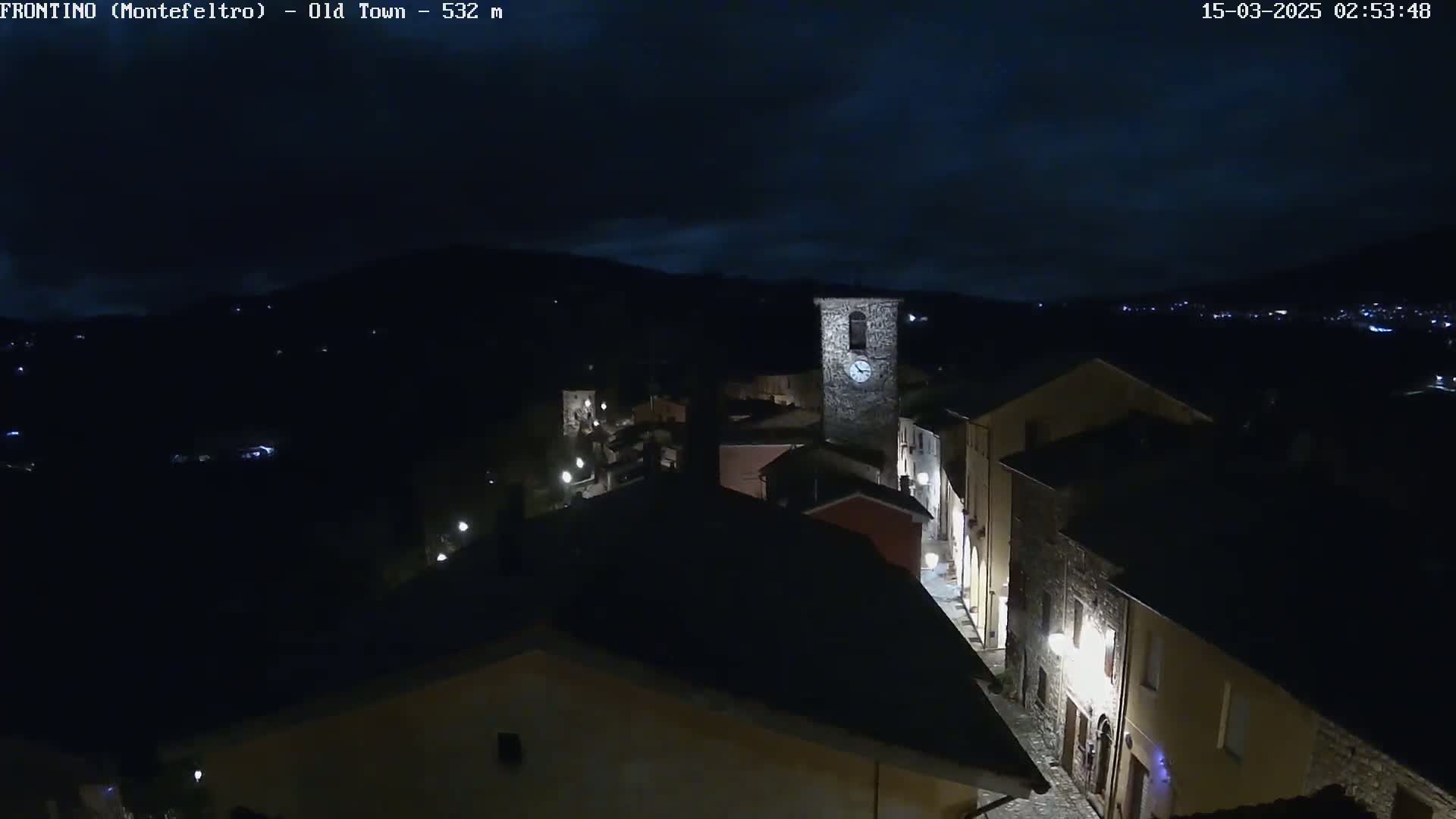 A nighttime, high-angle view of a small town nestled in a valley under a dark, cloudy sky.
