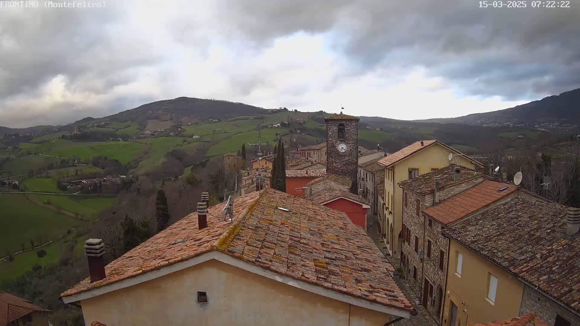 A view of a small village nestled in rolling green hills under a cloudy sky.