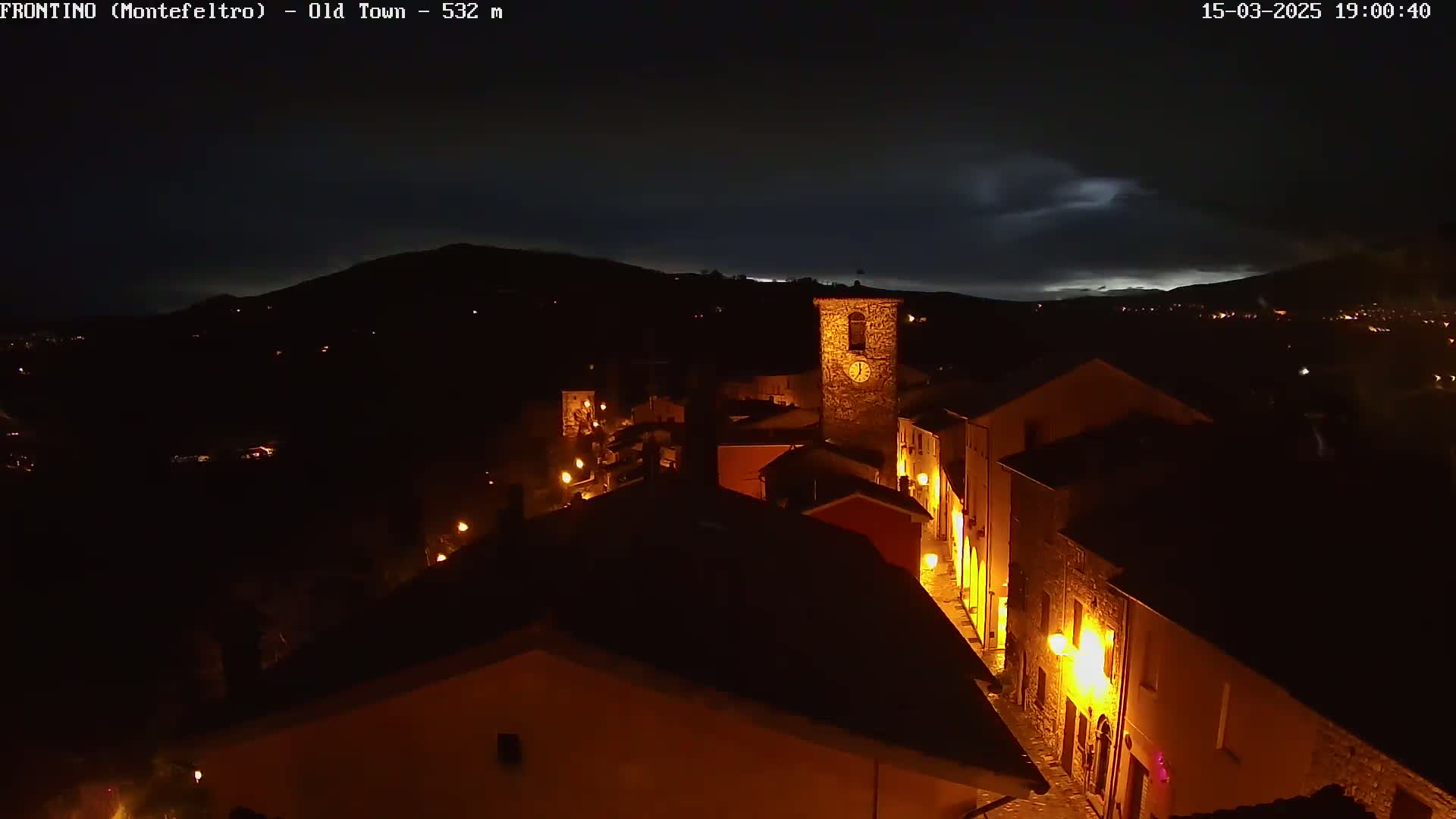 A nighttime view of a dimly lit town nestled in a valley under a dark, cloudy sky.