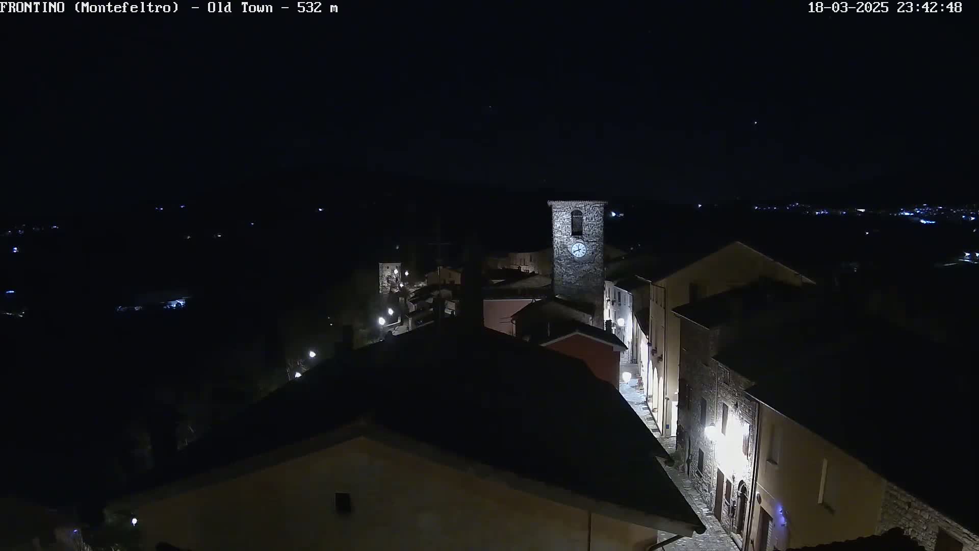 A nighttime, high-angle view shows a small, dimly lit town with a clock tower, under a clear, dark sky.