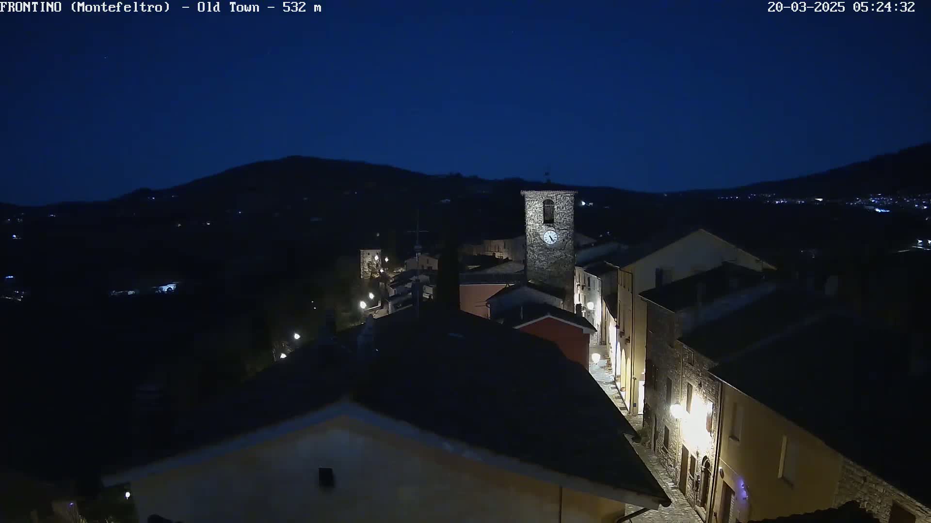 A nighttime, high-angle view of a dimly lit, small town nestled in a valley under a dark blue sky.