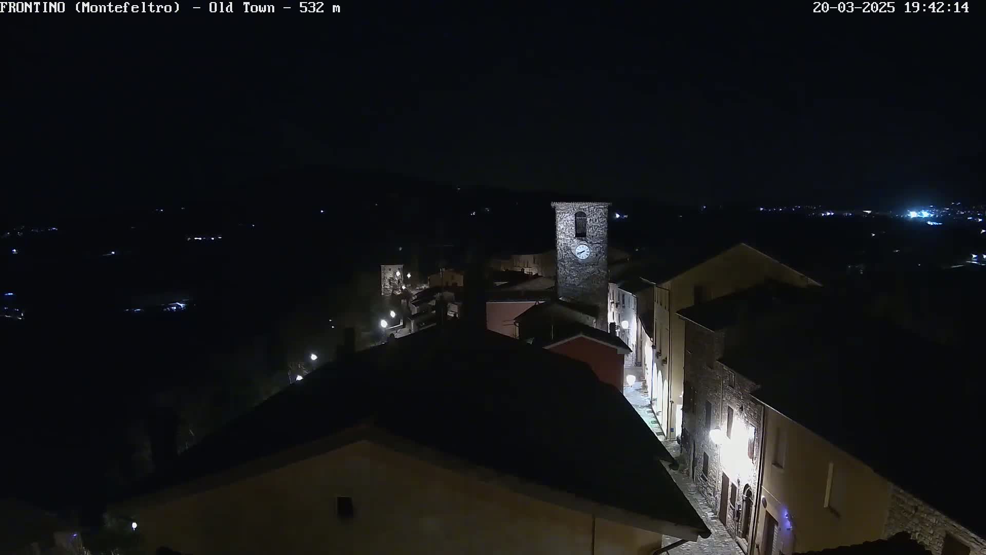 A nighttime, high-angle view of a small town with a clock tower, illuminated by streetlights.