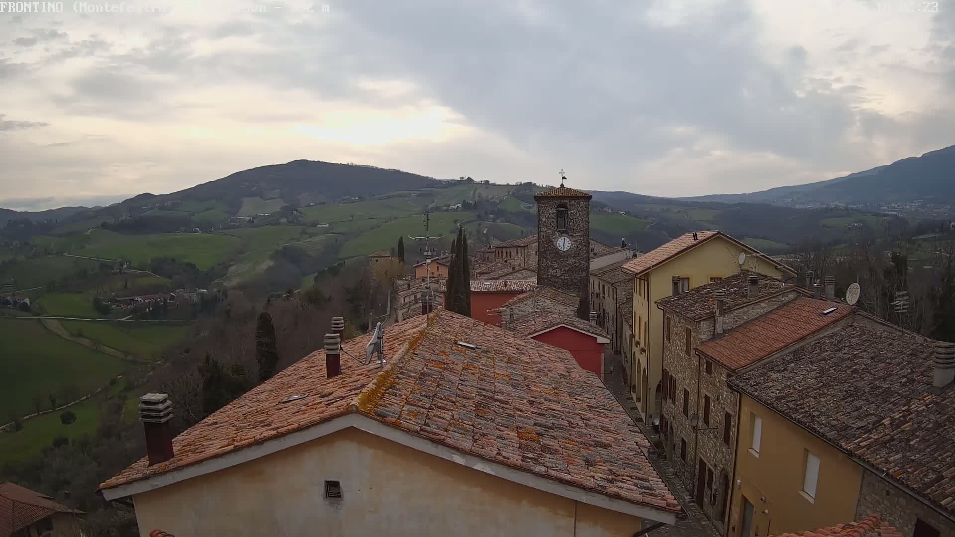 A village nestled in a valley overlooks rolling green hills under a cloudy sky.