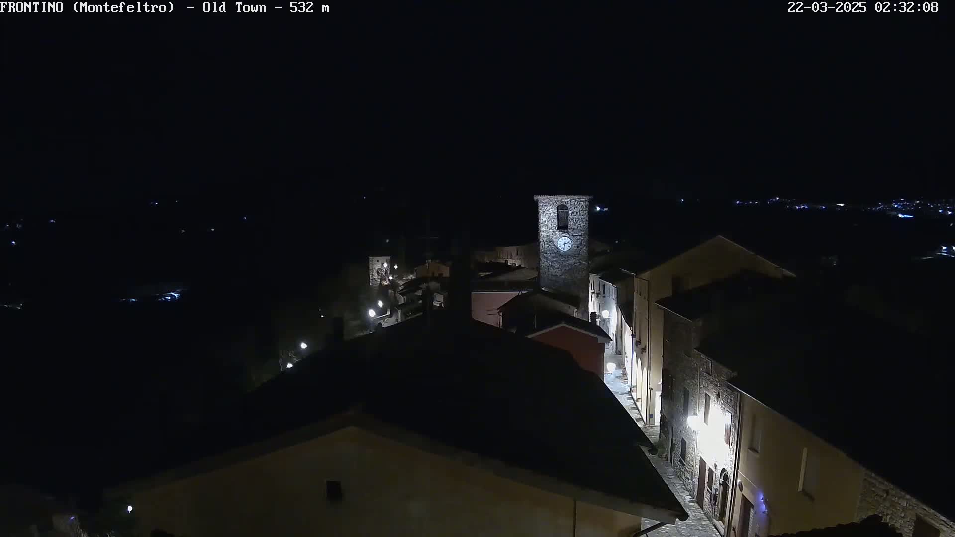 A nighttime, high-angle view shows a small town with stone buildings and streetlights illuminated against a dark sky.