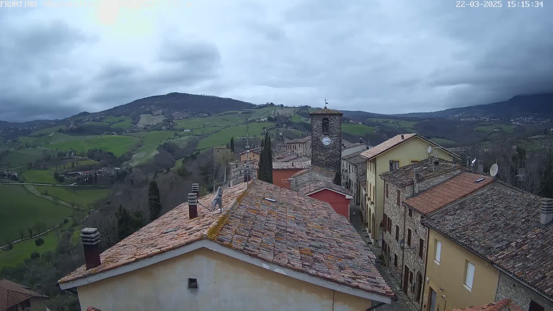 A stone village nestled in a green valley under a cloudy sky, with a clock tower prominent in the center.
