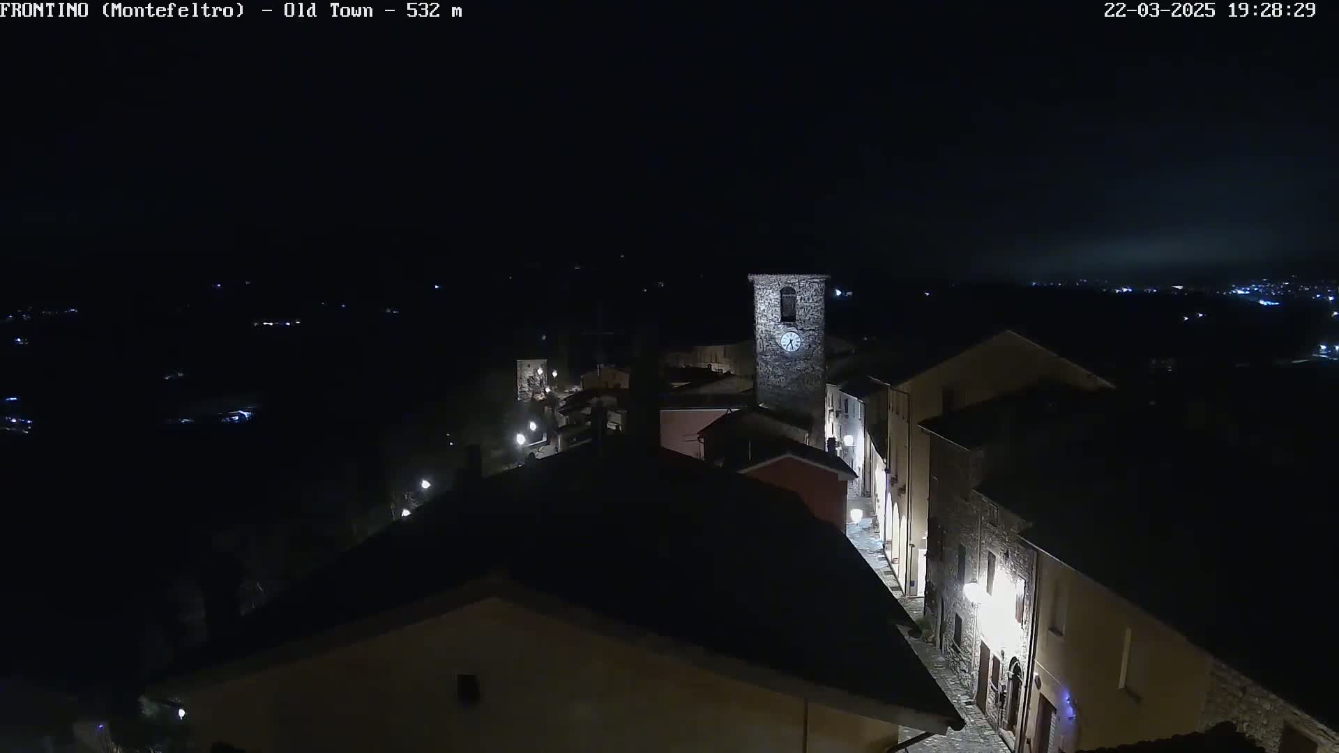 A nighttime, high-angle view shows a small, illuminated town nestled in a dark landscape.