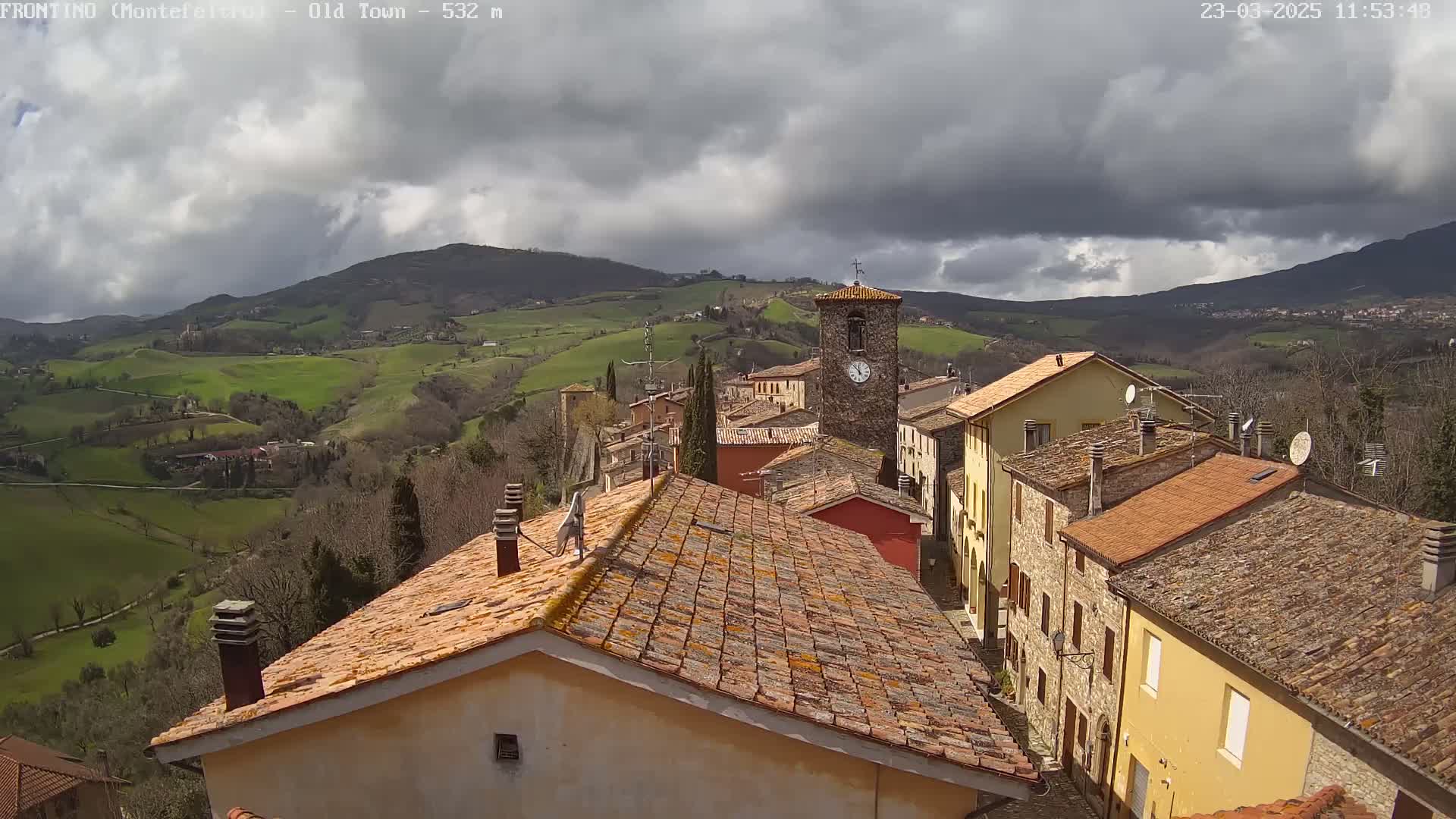 A small town nestled in rolling green hills under a mostly cloudy sky.