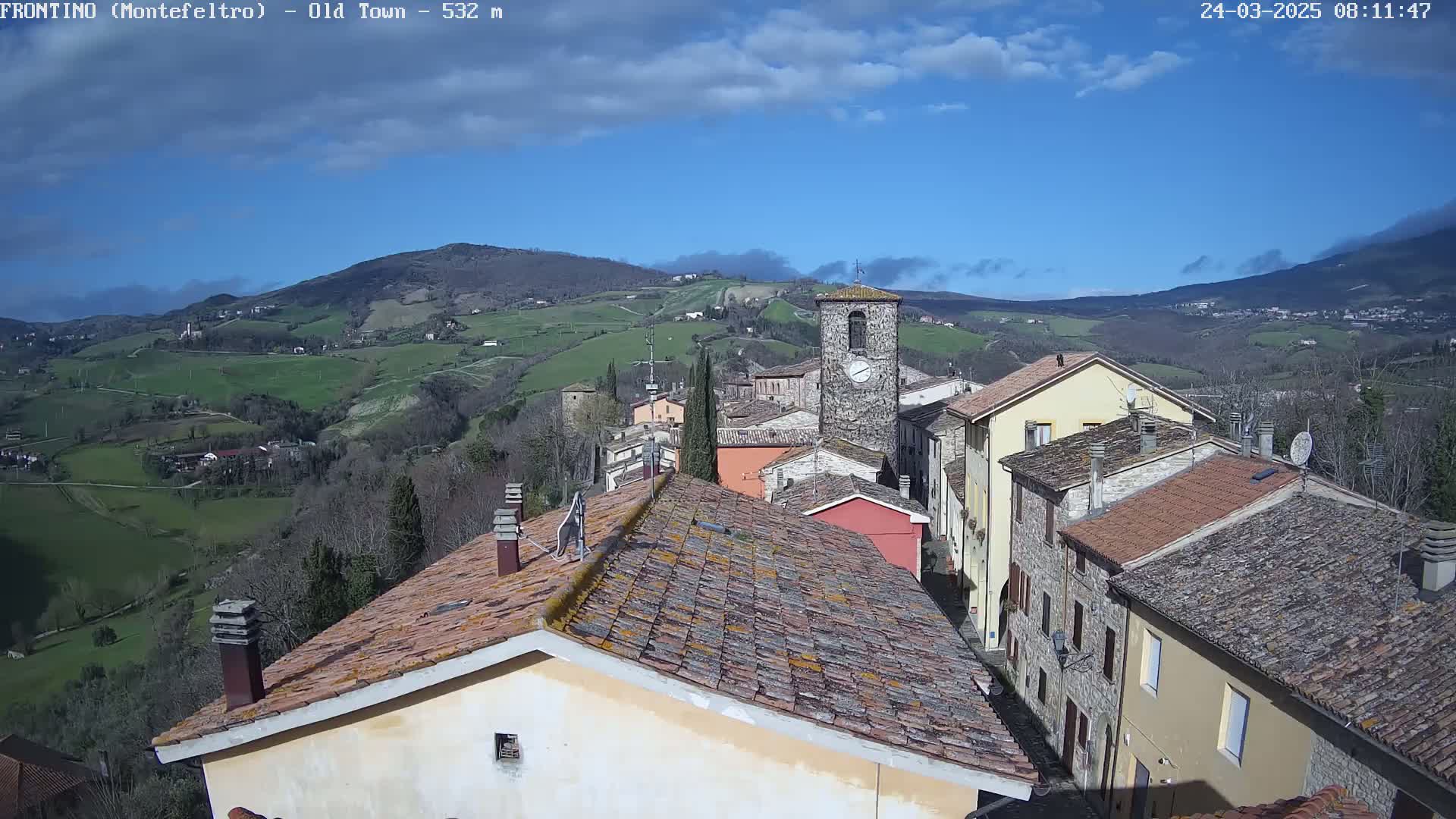 A view of a small town nestled in a valley, under a mostly clear blue sky with a few clouds.