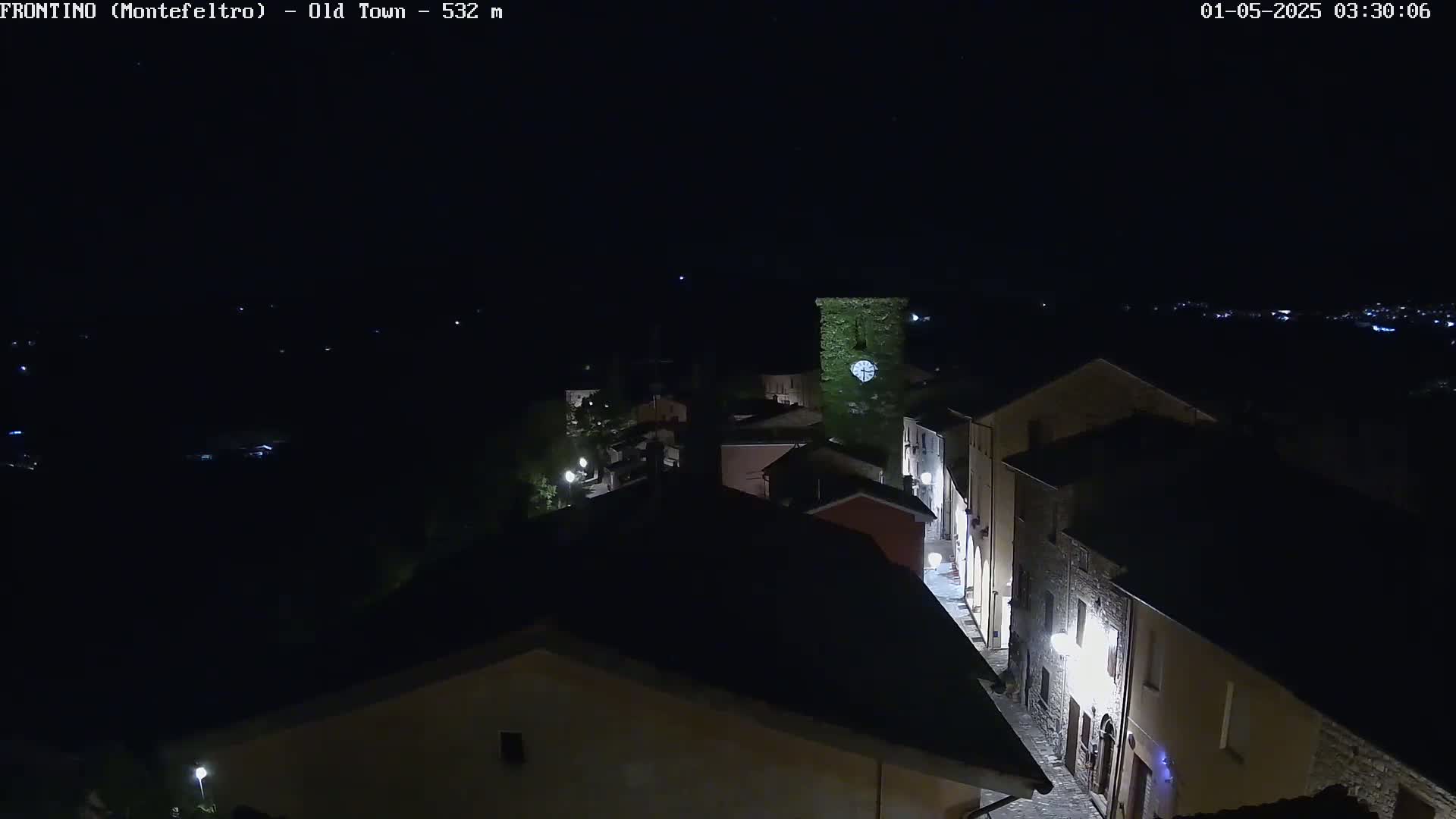 A nighttime, high-angle view of a small, dimly lit town with stone buildings and a few streetlights.