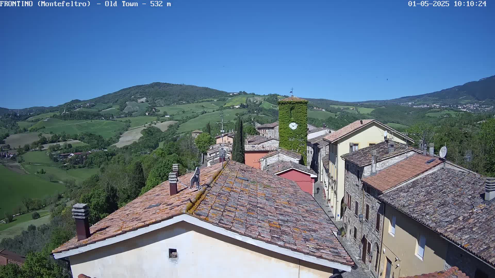 A quaint village nestled in a valley under a clear blue sky, surrounded by rolling green hills.