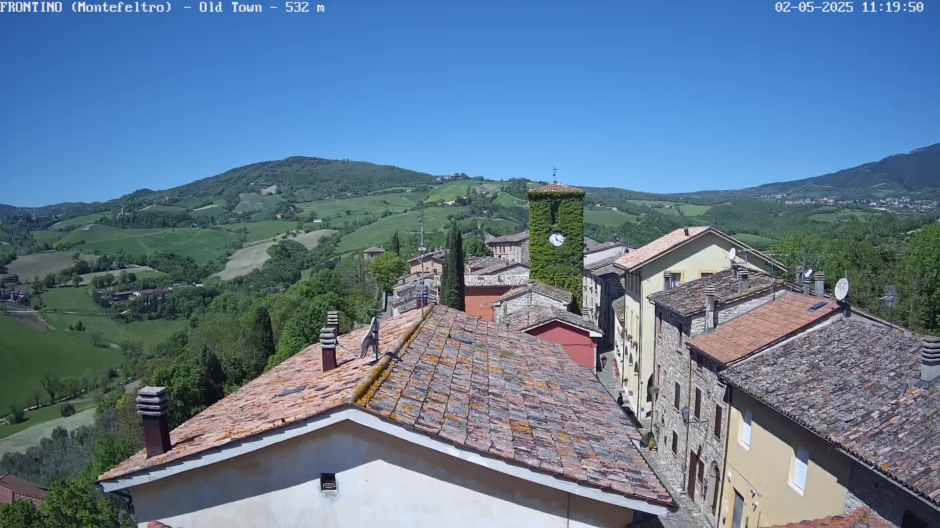 A sun-drenched view of a quaint village nestled in a verdant valley, under a clear blue sky.