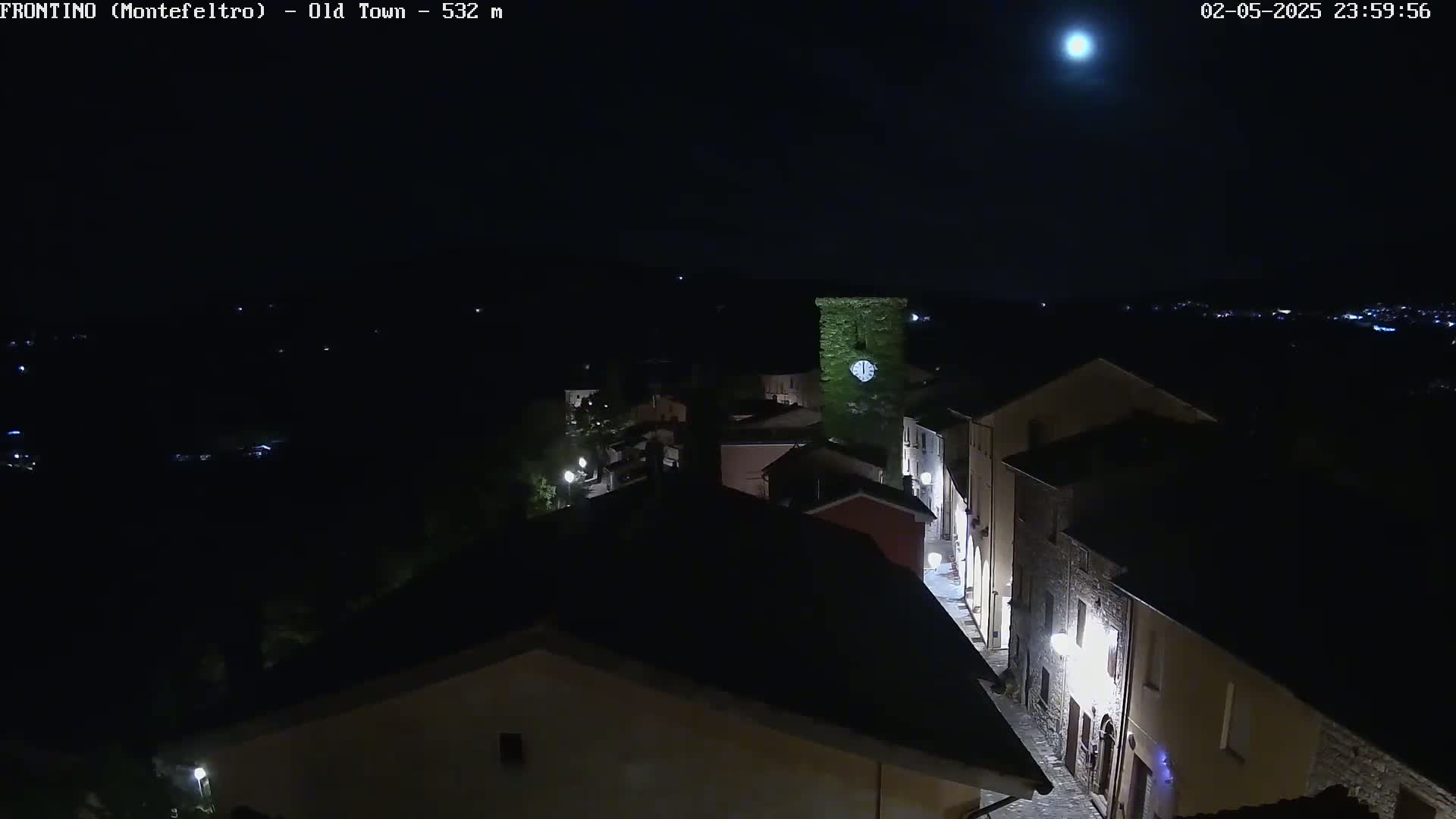 A brightly lit moon illuminates a nighttime view of a small town nestled in a dark landscape.