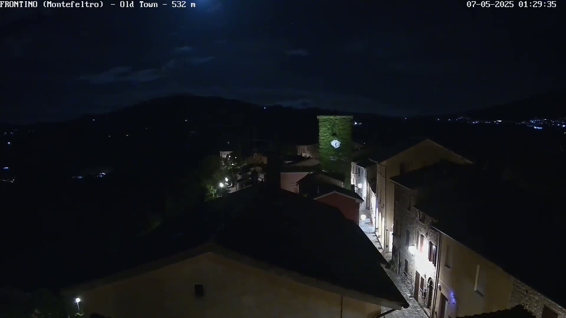 A nighttime, high-angle view of a dimly lit, stone village nestled in a dark landscape under a mostly clear sky.