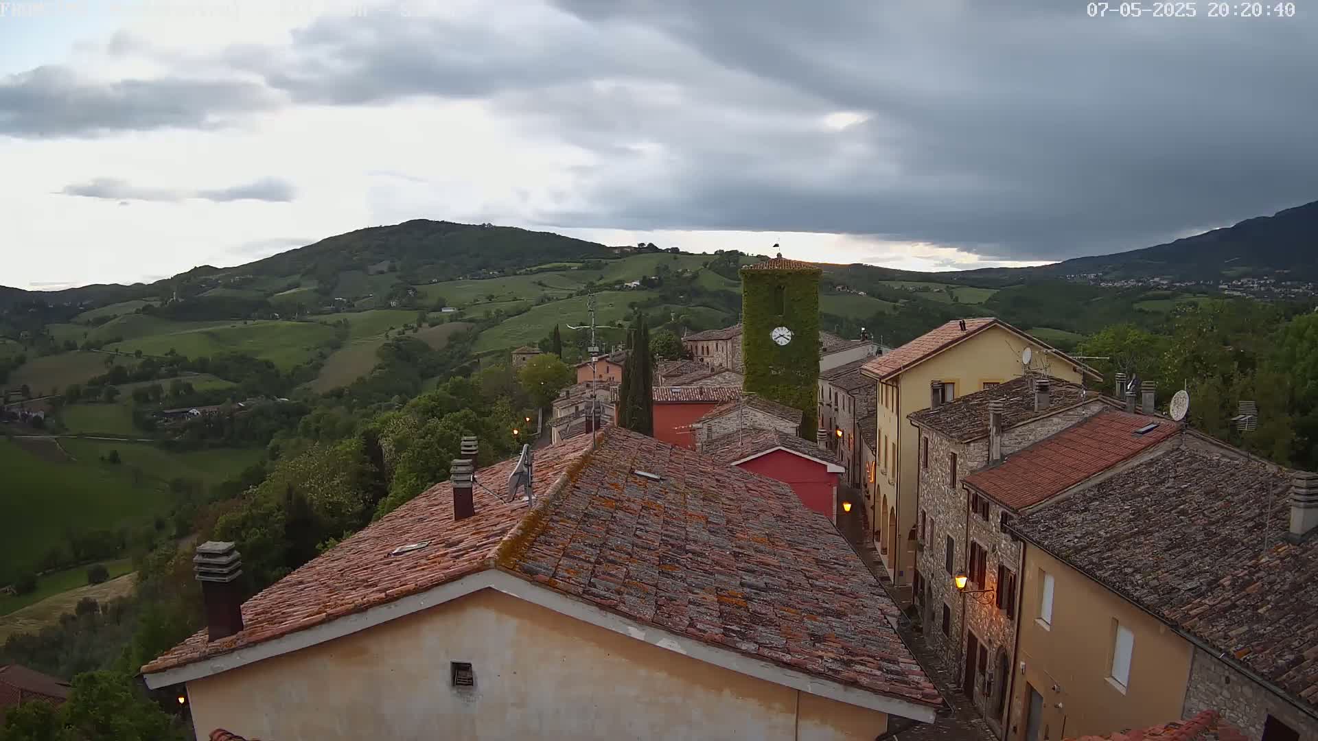 A small village with terracotta roofs nestles in a verdant valley under a partly cloudy sky.