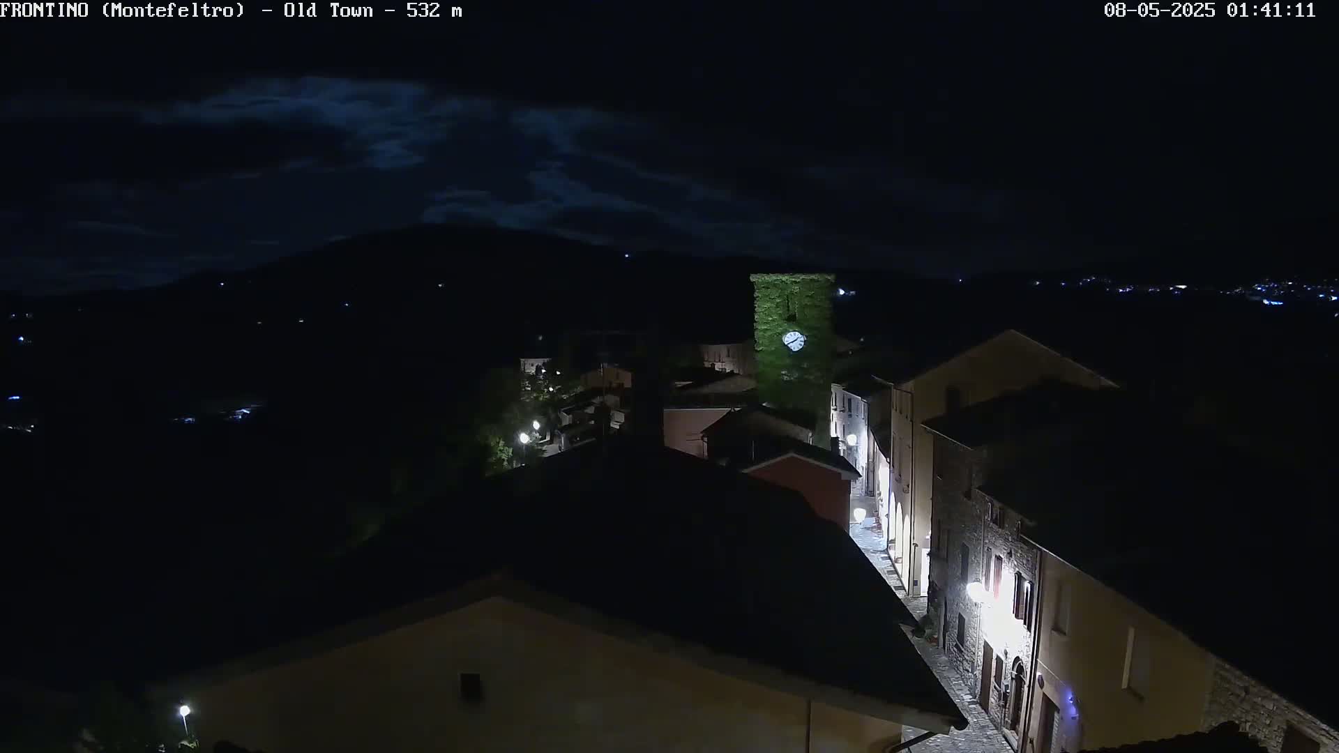 A nighttime, high-angle view of a small town nestled in a valley under a partly cloudy sky.