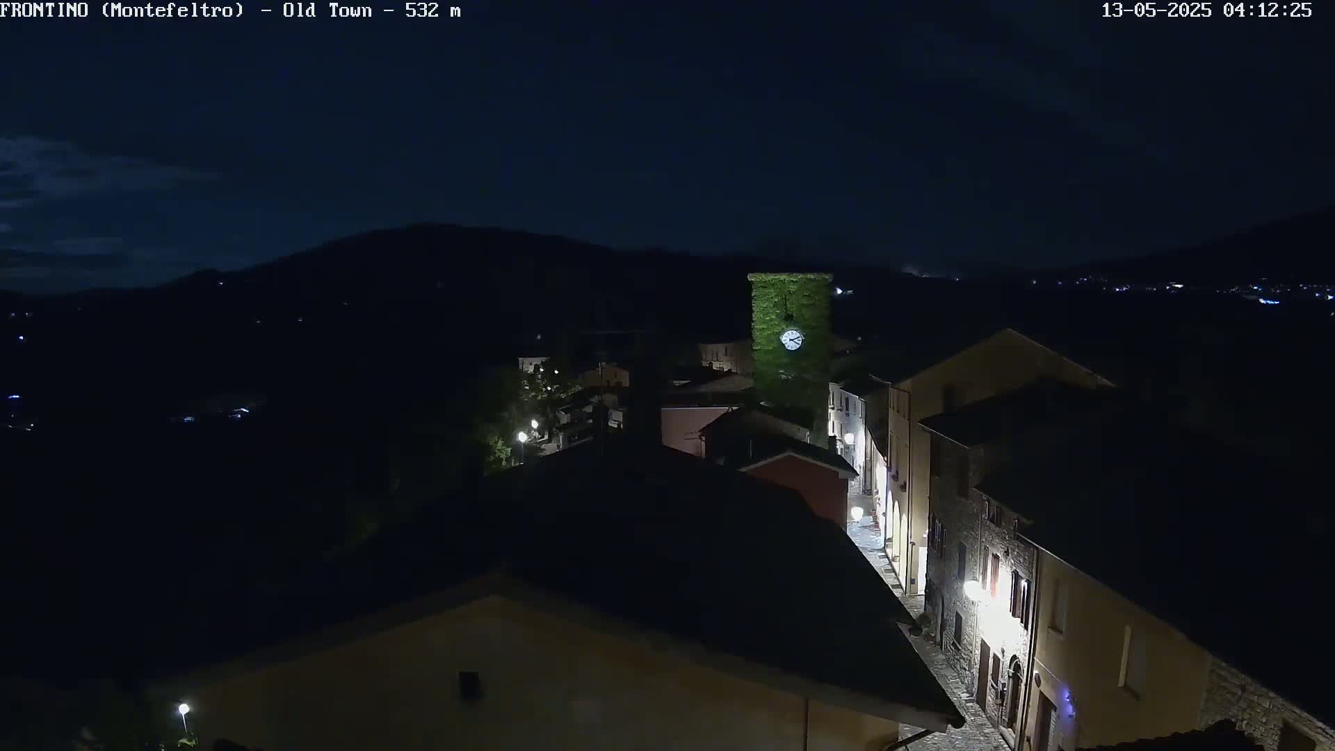 A nighttime, high-angle view shows a small town nestled in a valley, illuminated by streetlights against a dark sky.