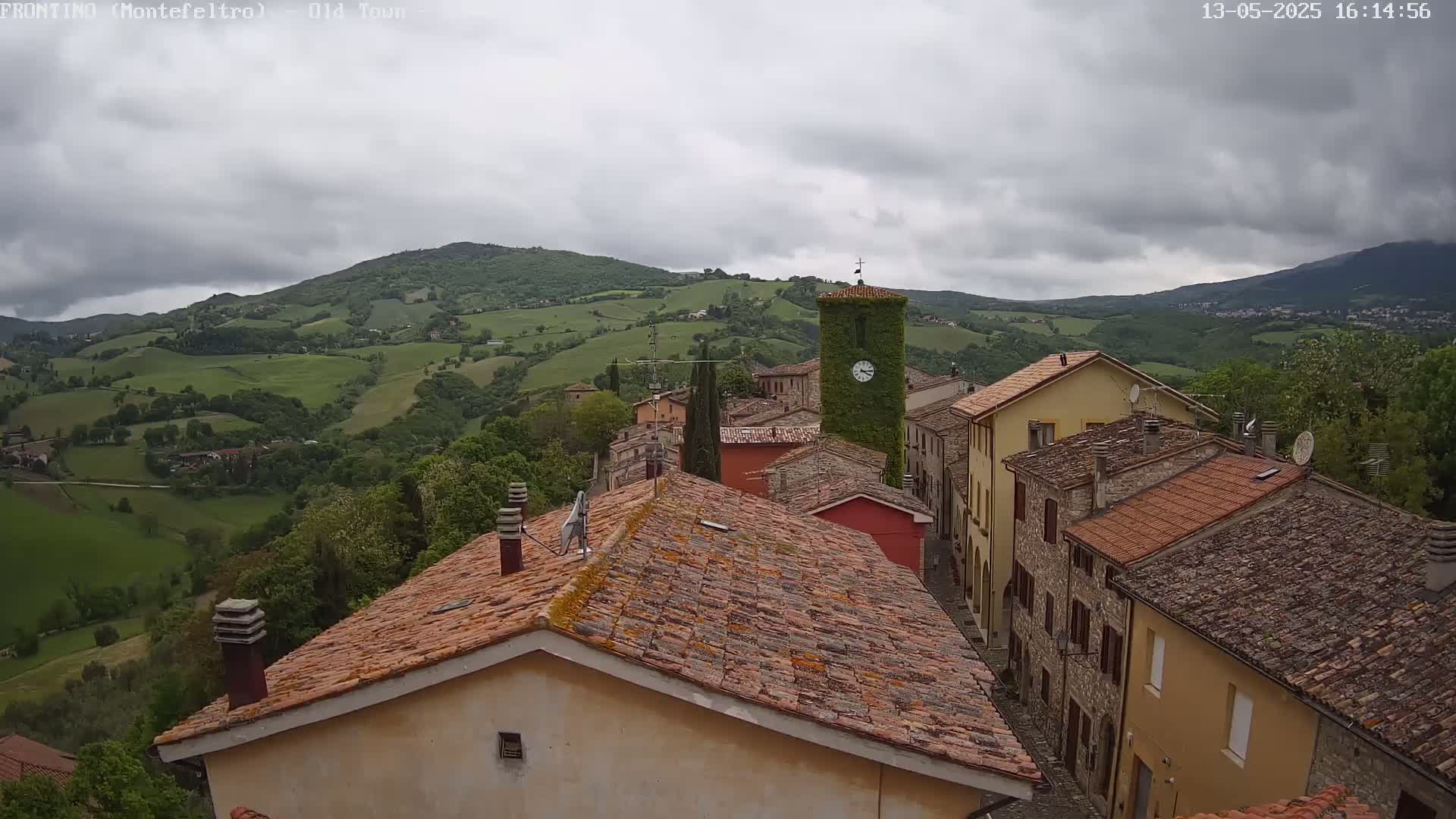 A view of an old town nestled in a valley, with terracotta-roofed buildings under a cloudy sky.