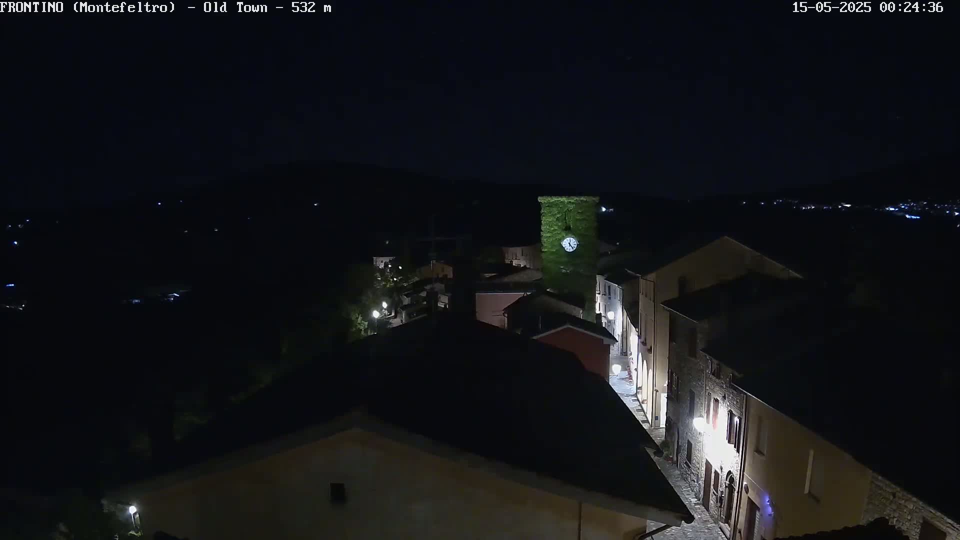 A nighttime, high-angle view of a small town's old town, illuminated by streetlights, with a clock tower visible in the center.