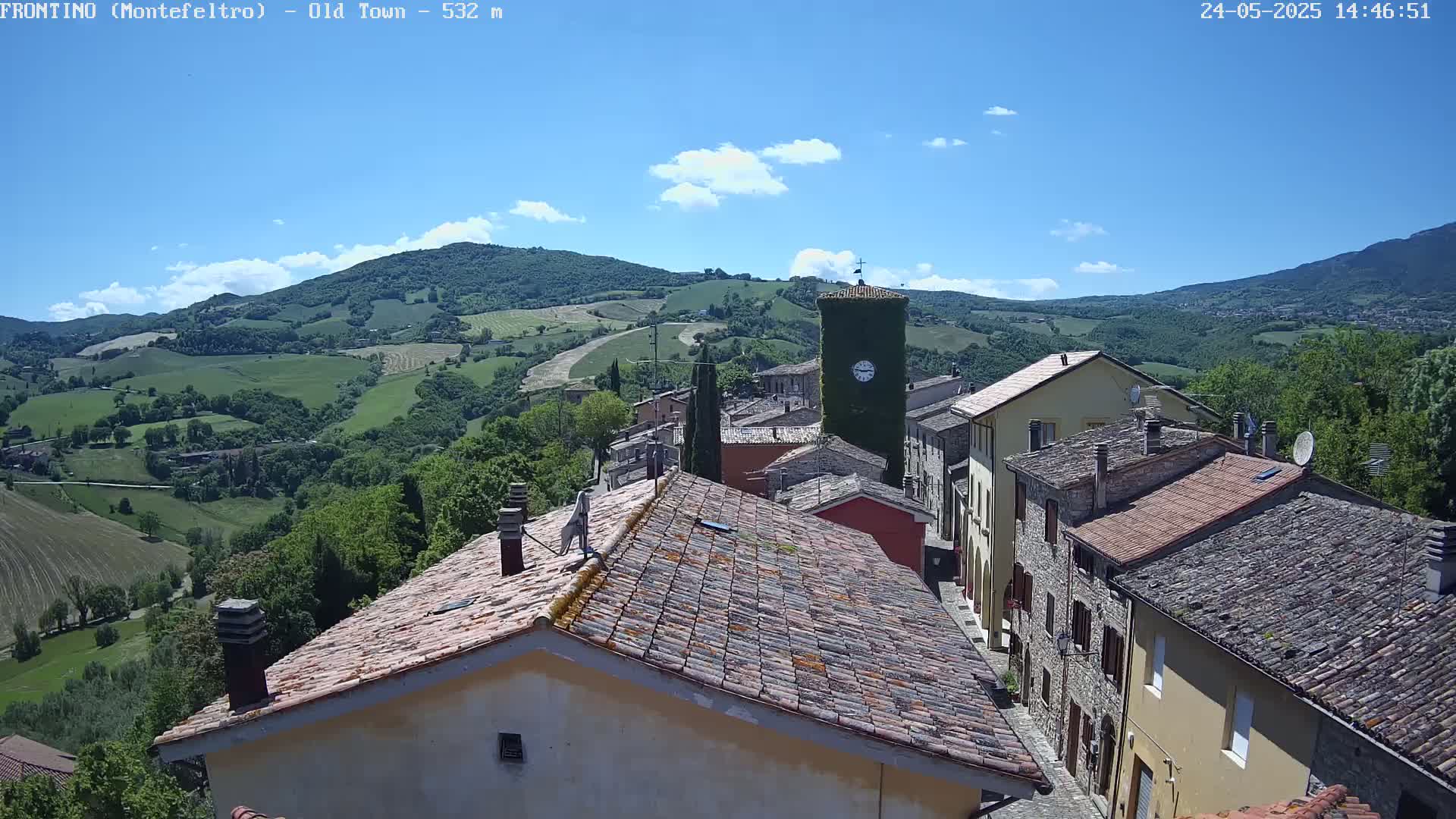 A quaint, stone-roofed village nestled in a verdant valley under a mostly sunny sky.
