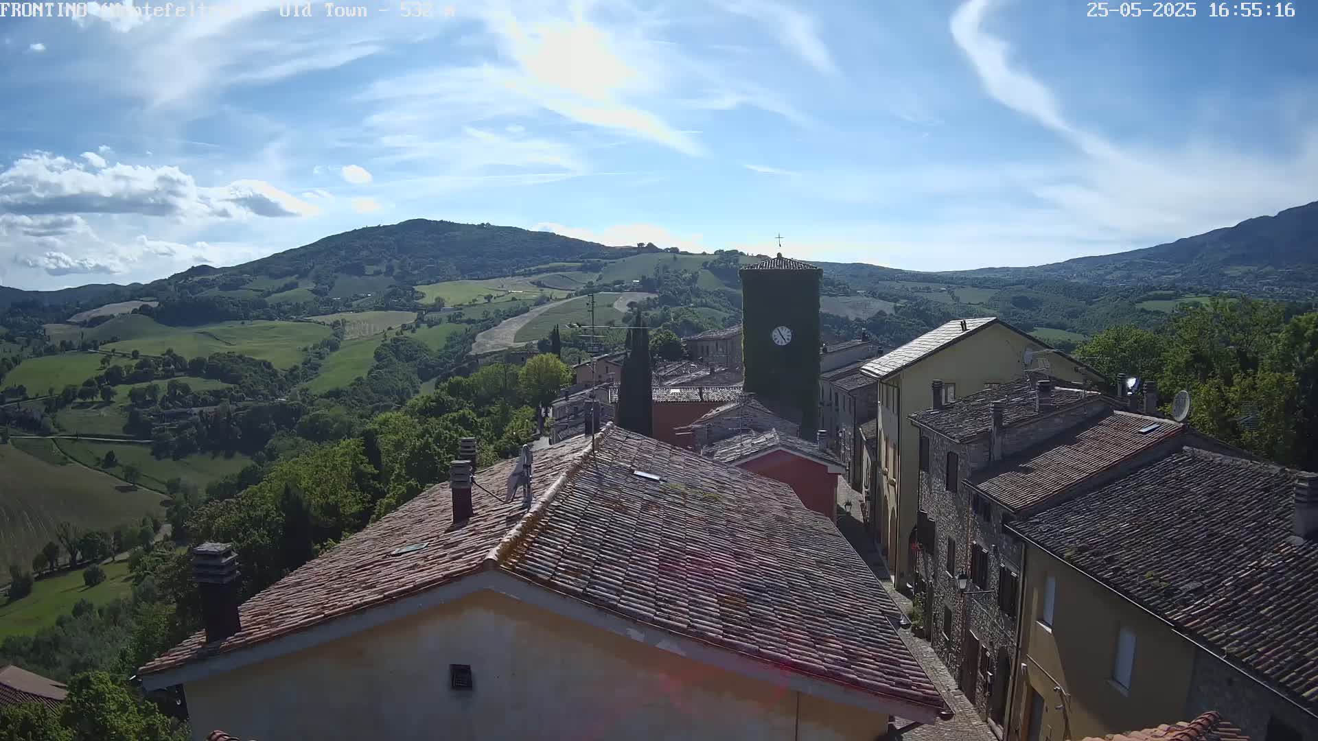A mostly sunny day reveals a quaint village nestled in a valley, overlooked by rolling green hills.