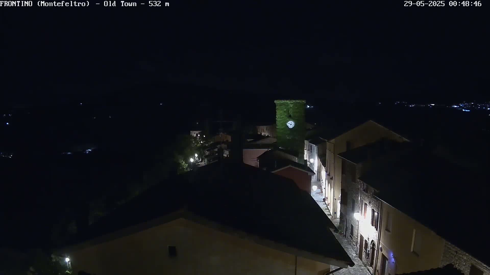 A nighttime, high-angle view of a small town with a clock tower, illuminated by streetlights.