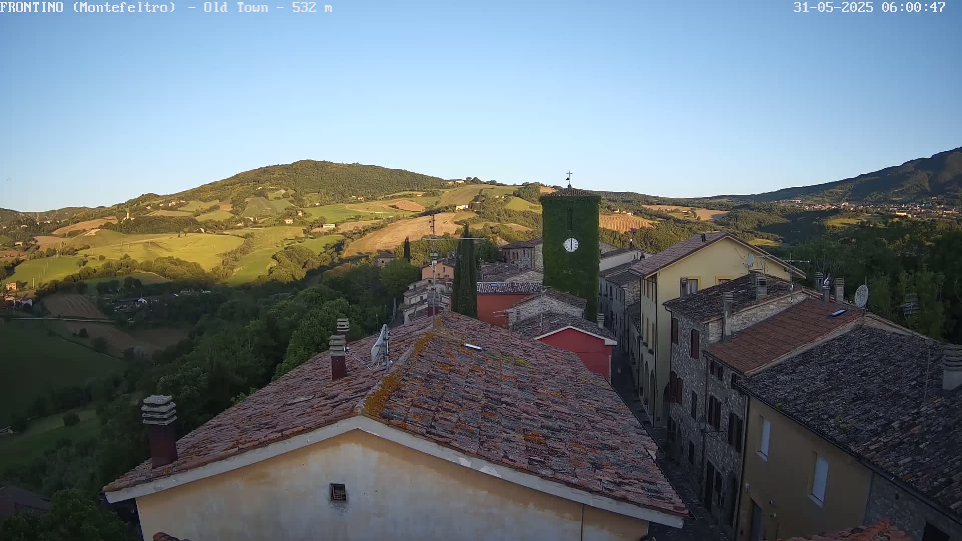 A small village nestled in a valley overlooks rolling green hills under a clear blue sky.