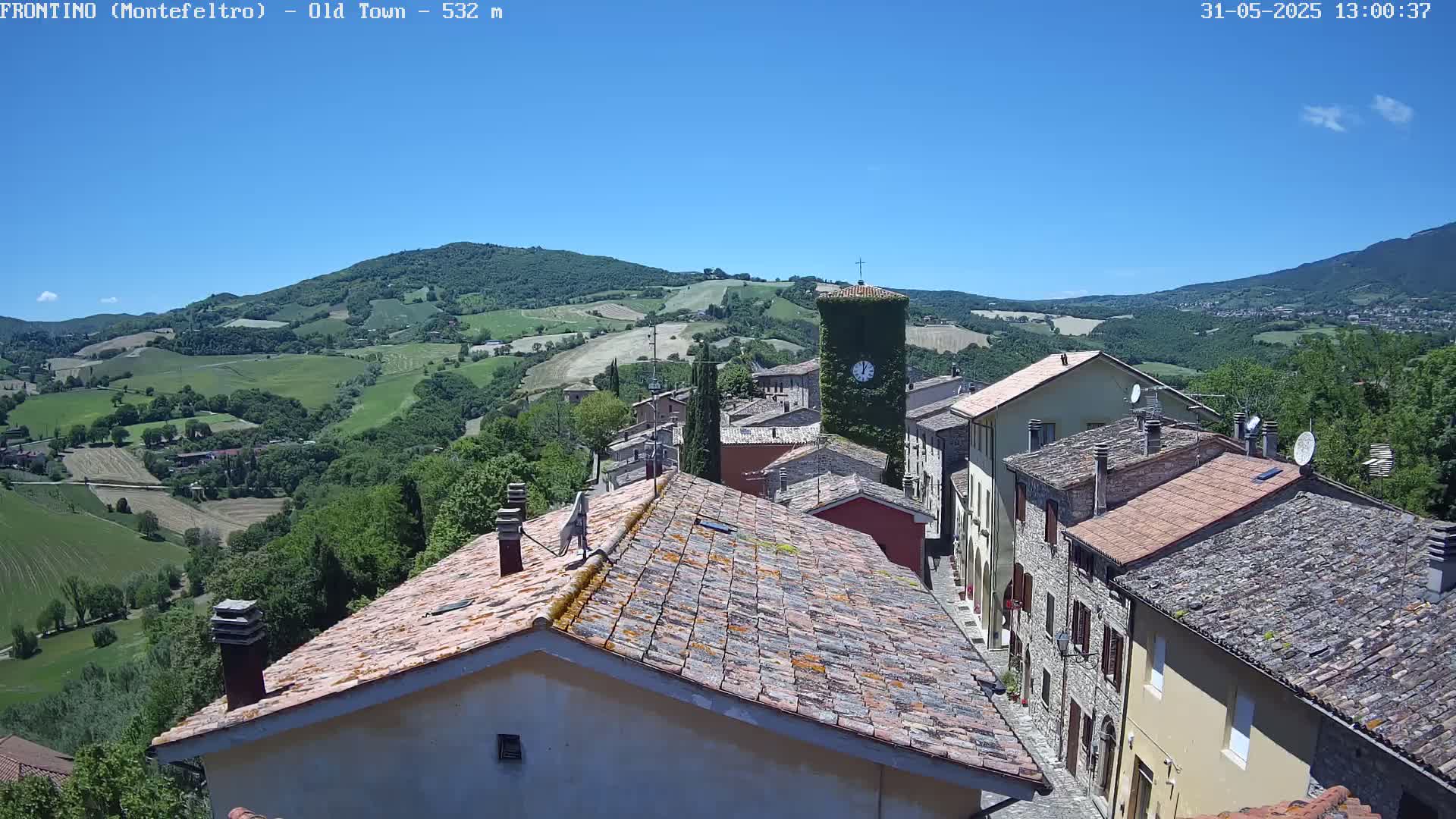 A picturesque village nestled in a valley under a clear blue sky, surrounded by rolling green hills.