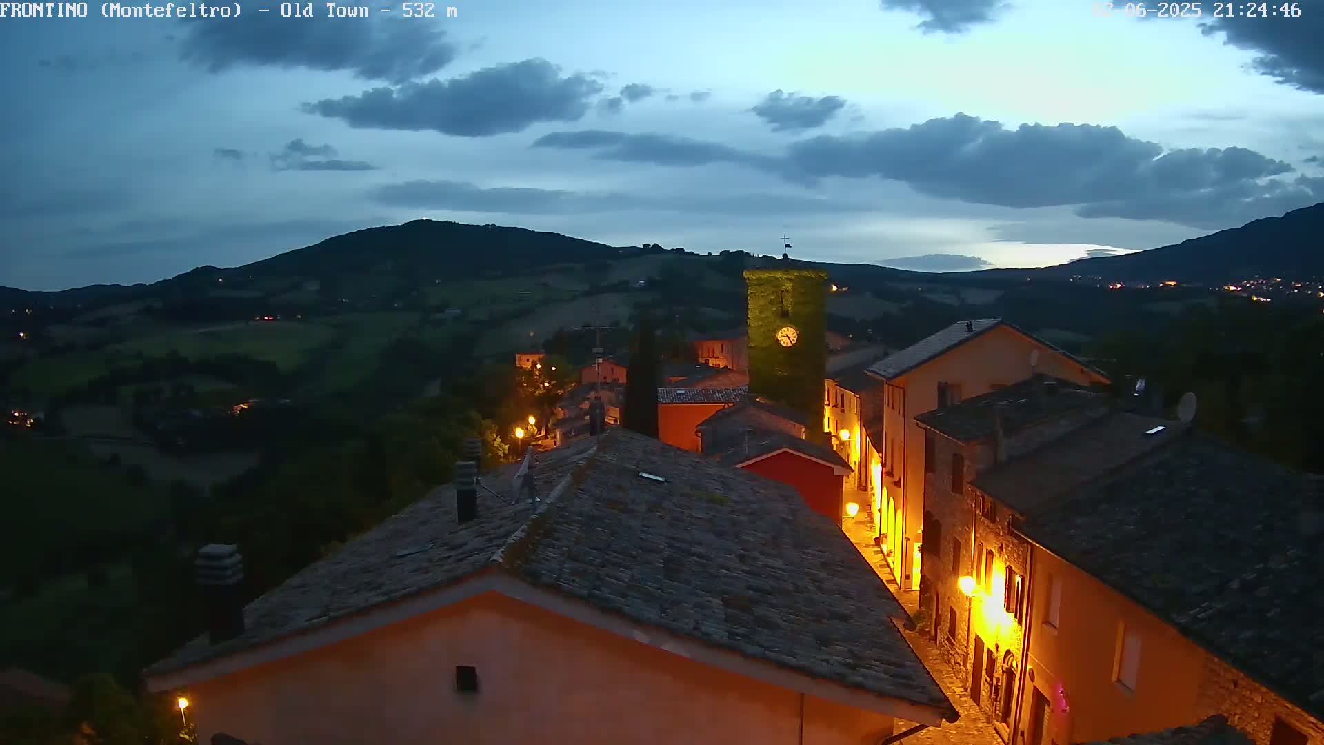 A nighttime view of a small, illuminated town nestled in a valley under a partly cloudy sky.