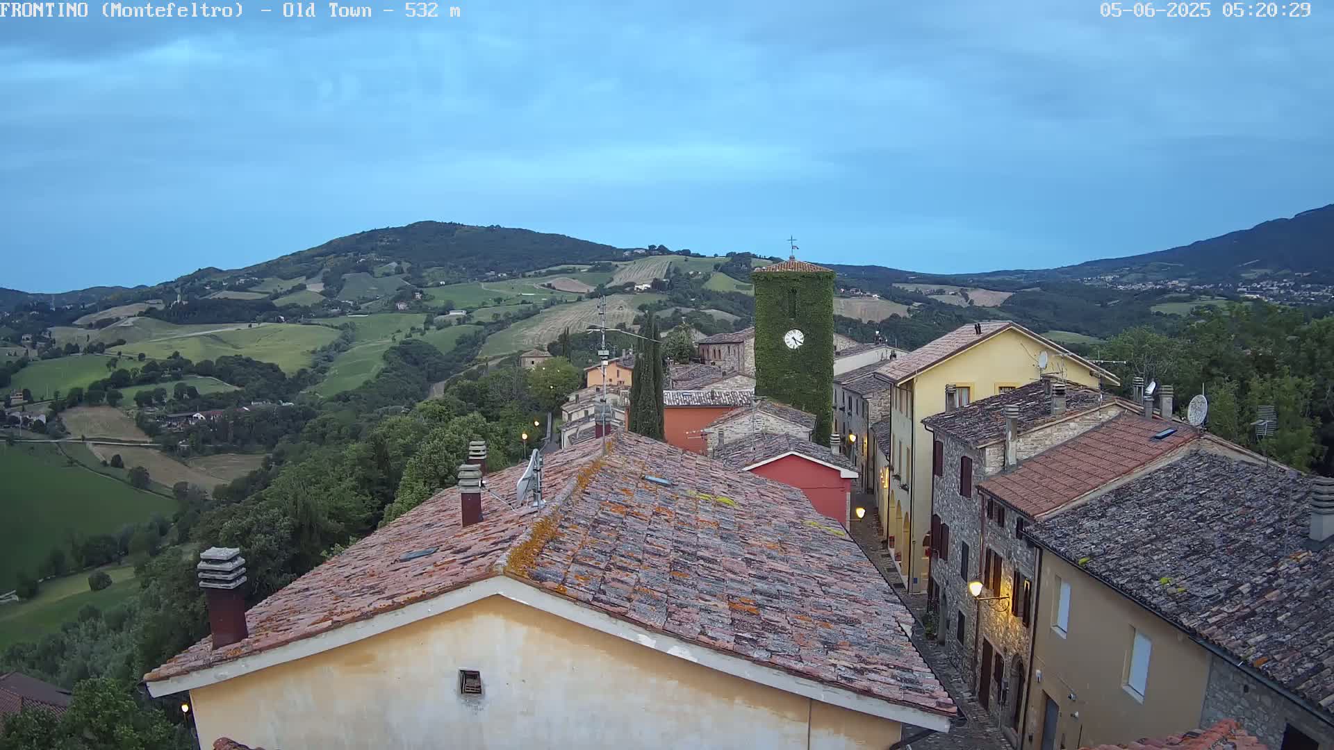 A small town nestled in a valley, under a twilight sky, is surrounded by rolling green hills.