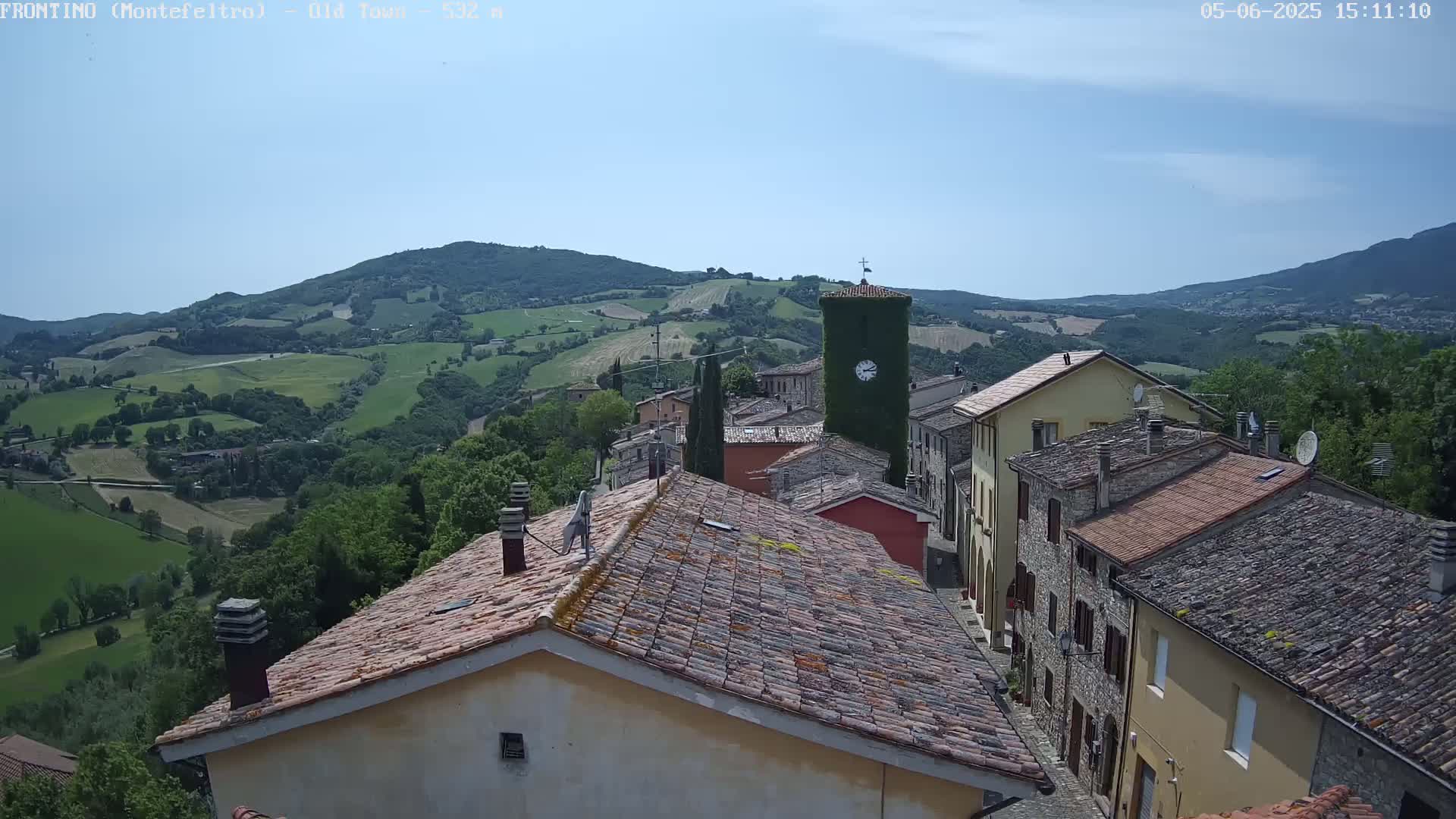 A view of a small town nestled in a hilly, green landscape under a clear, sunny sky.