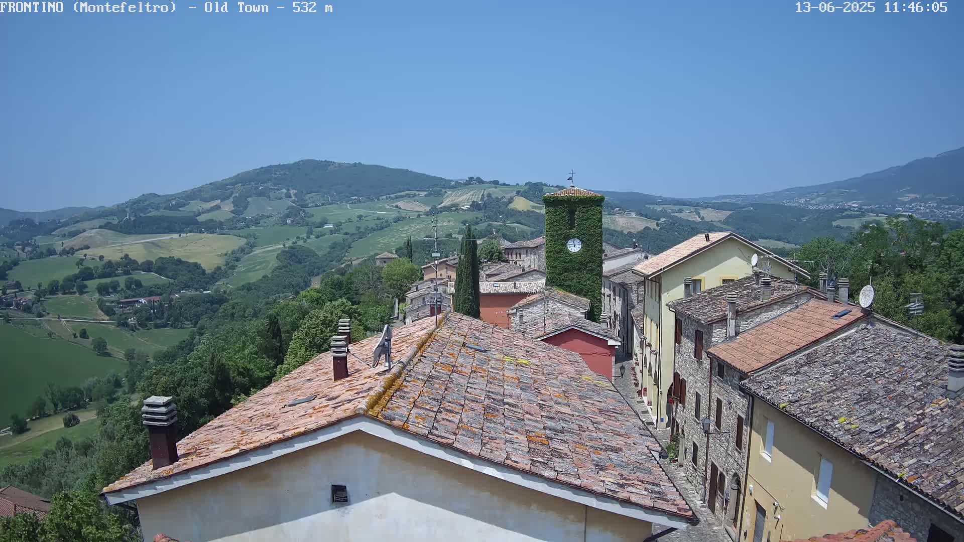 A view of a small town nestled in a valley on a clear, sunny day, with rolling hills and mountains in the distance.