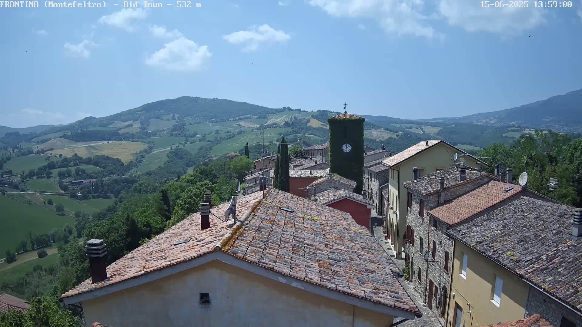 A picturesque village nestled in a hilly landscape under a mostly sunny sky, with a clock tower prominent in the scene.