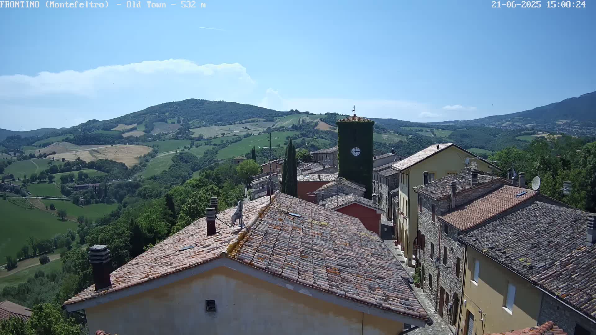 A picturesque village nestled in a valley under a clear blue sky, with rolling green hills and mountains in the background.