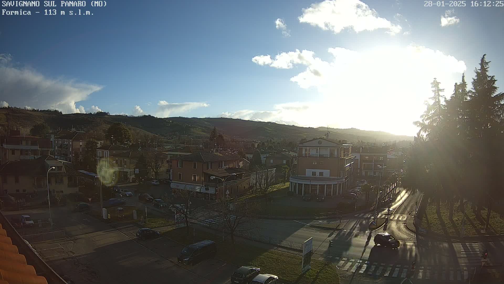 A sunny day with some clouds over a town nestled in a valley, with cars parked along streets and roads intersecting.