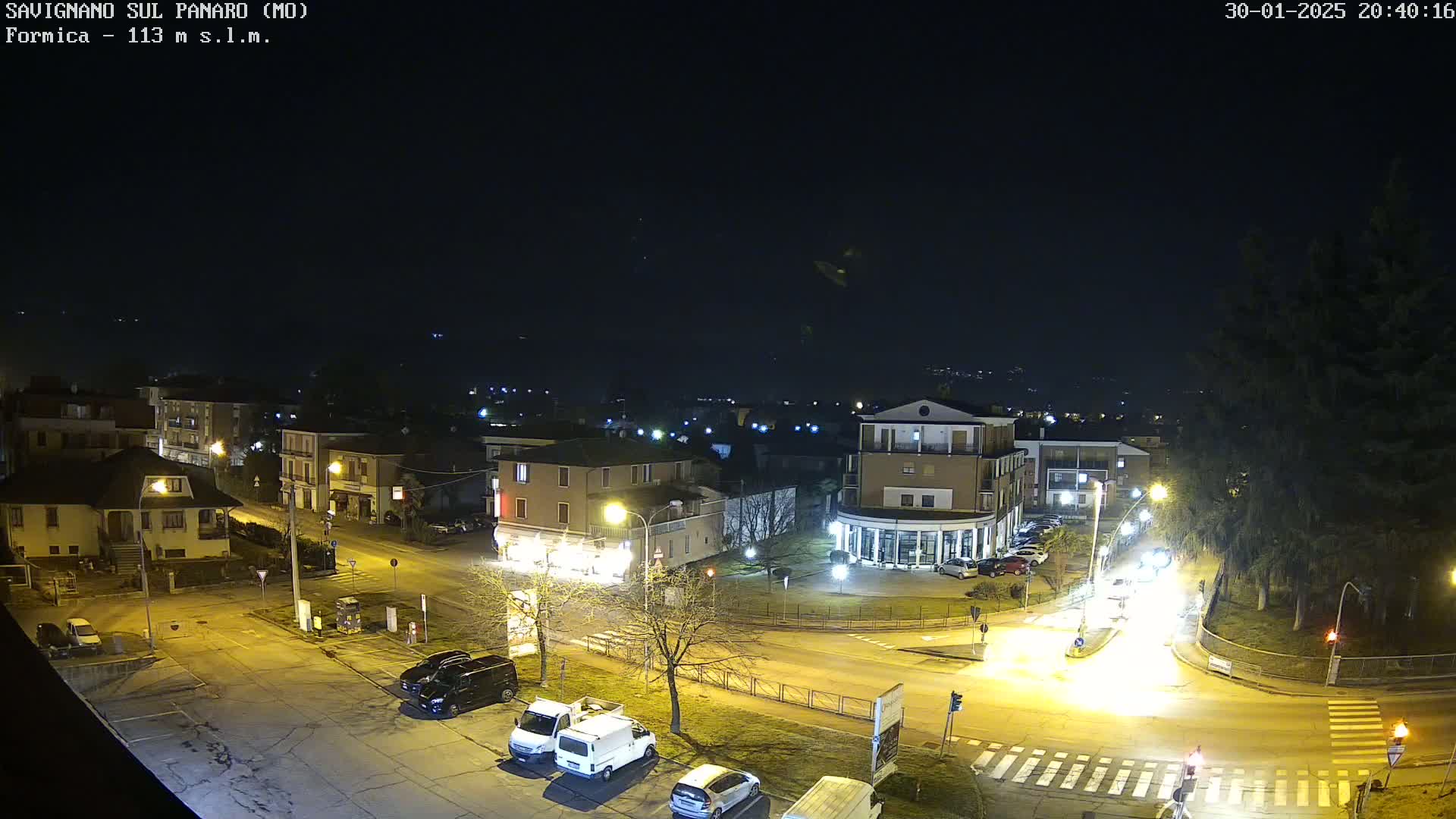 A nighttime, high-angle view of a town square with several cars and buildings illuminated by streetlights.
